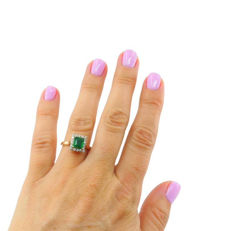 Ein Smaragdring aus 14-karätigem Gold, mit Diamanten besetzt.u2028 In der Mitte befindet sich ein quadratischer, leuchtend grüner Smaragd, umgeben von einem Halo aus Diamanten. 
Dieser Ring im Vintage-Stil hat einen geometrischen Schwerpunkt und