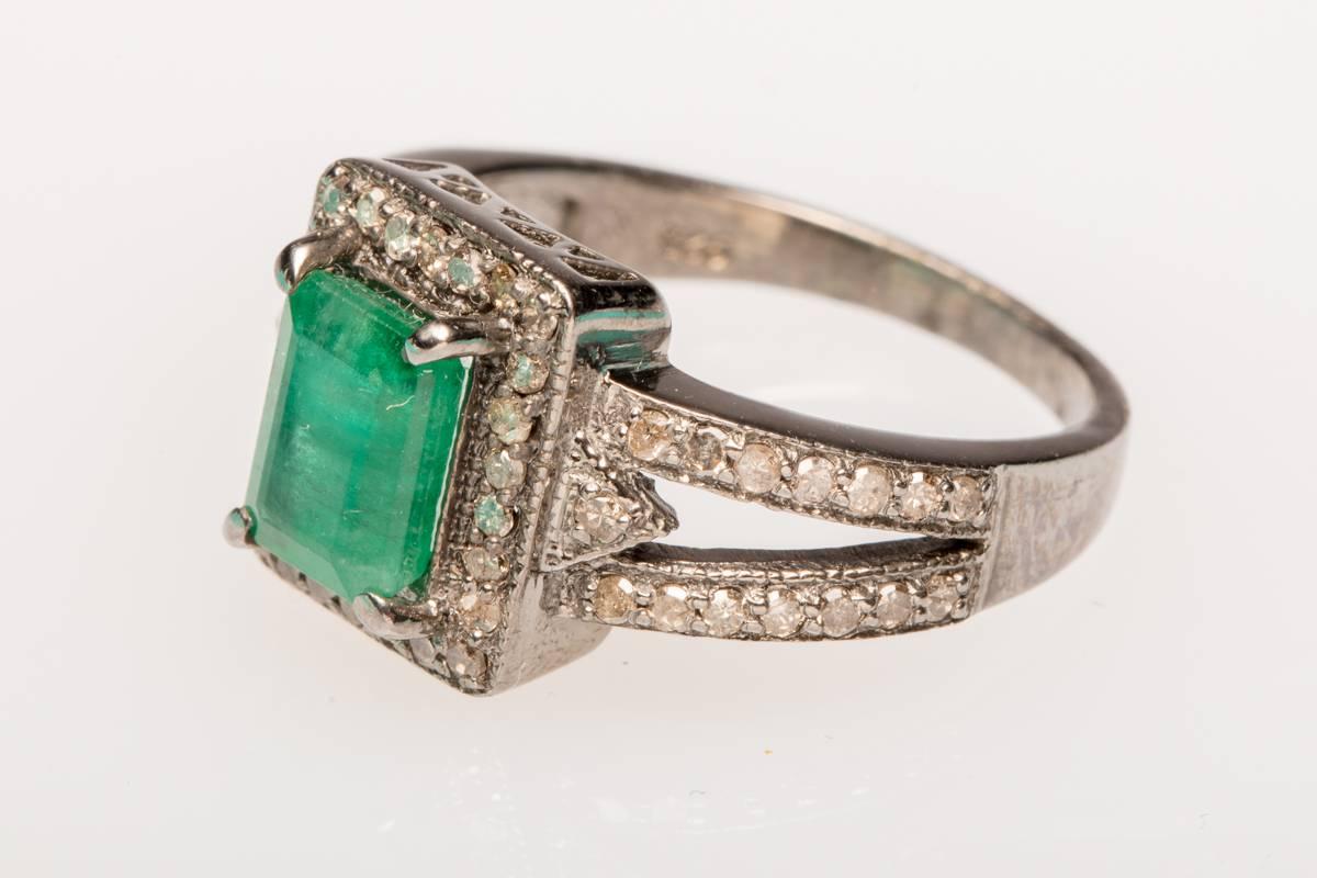 An emerald cut, emerald ring bordered in pave`-set diamonds, as well as along the top part of the band.  Set in oxidized sterling silver.  Carat weight of emerald is 1.67; diamonds .65.  Ring size is 7.5.