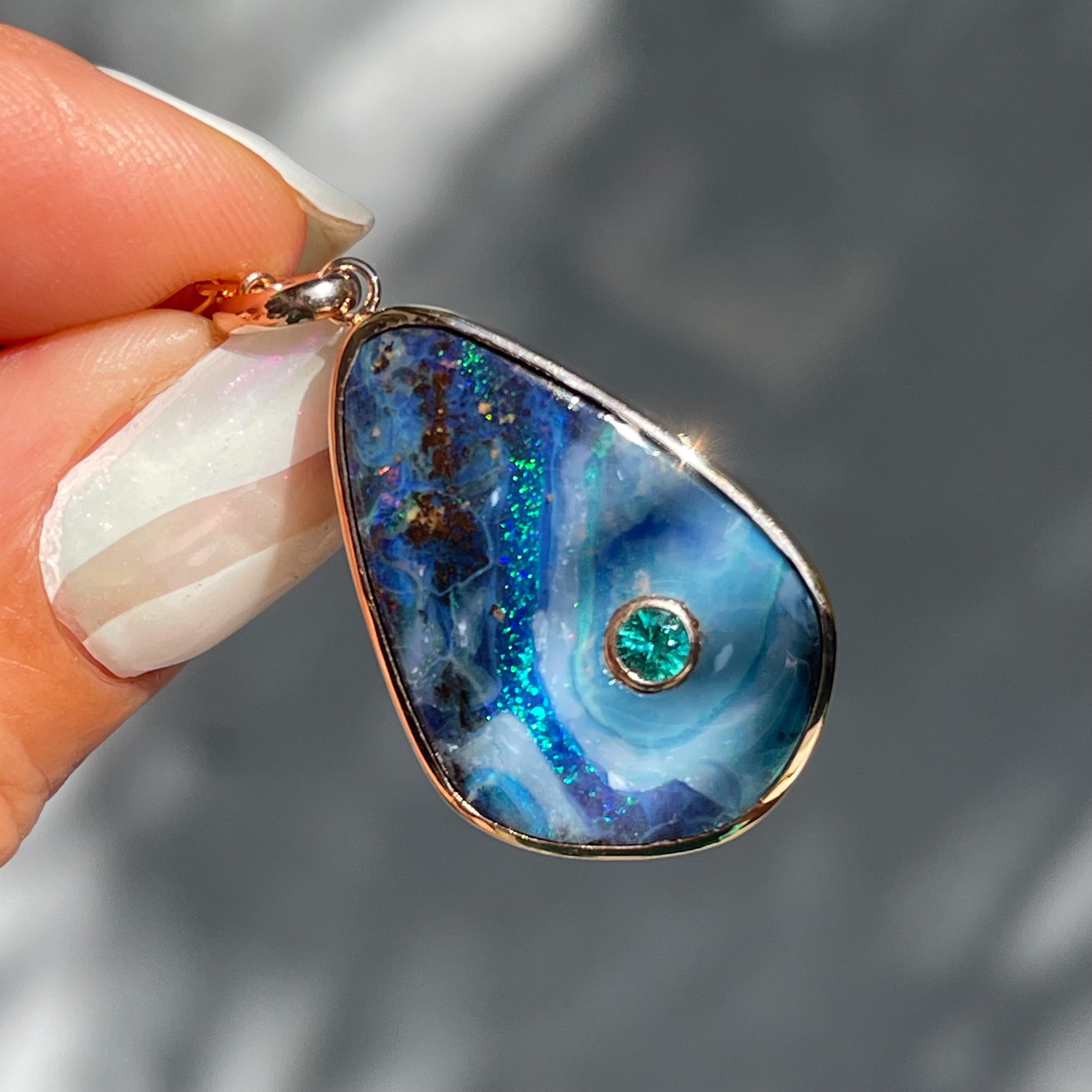 Inside this Australian Opal Necklace flows a scintillating river with emerald hues. Embedded in the scenic blue opal is a glistening emerald anchoring the opal pendant. The sinuous river meanders around the verdant gem, pursuing the path of least