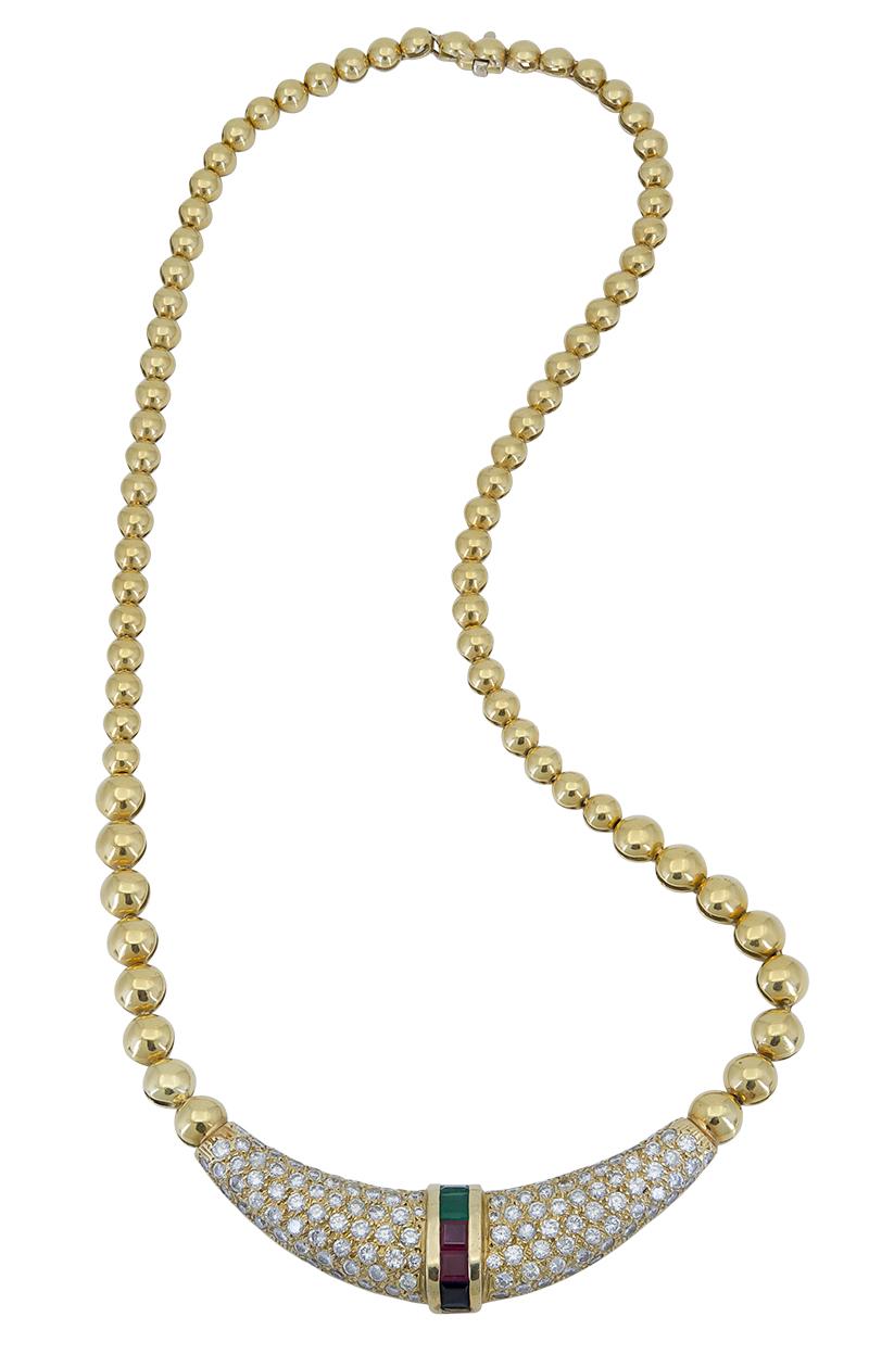 Collar estilo gargantilla realizado en oro amarillo que luce un colgante en forma de boomerang micropavé engastado con diamantes brillantes redondos. Acabado con una barra cuadrada de esmeraldas y rubíes engastada en el centro del colgante. 
El peso