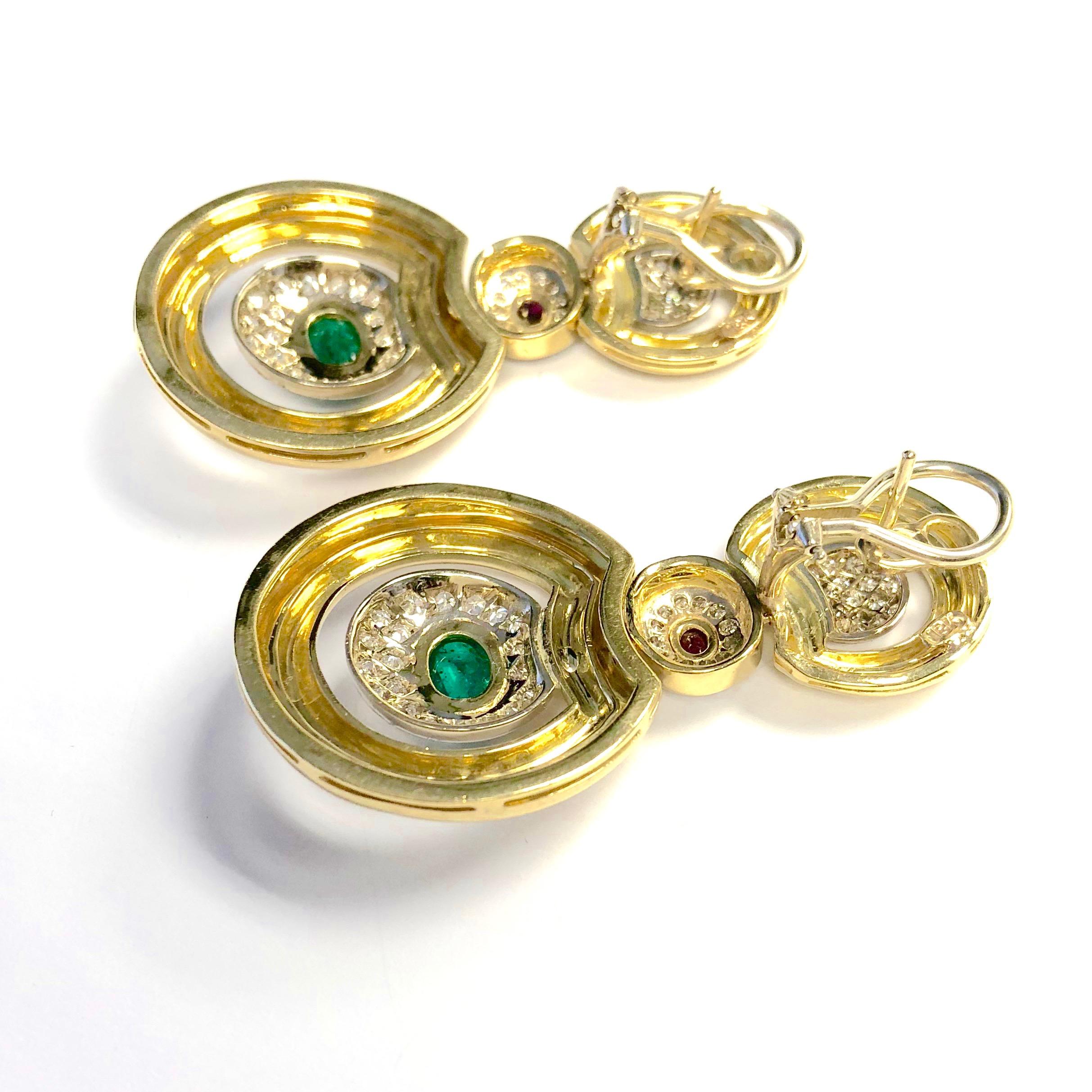 Crafted in 18K yellow gold, each earring features a circular design with emerald, ruby and diamond accents. Post and omega backings for added security. 
2 bezel set oval cabochon emeralds: approximate total weight of 2.00ct
2 bezel set oval cut