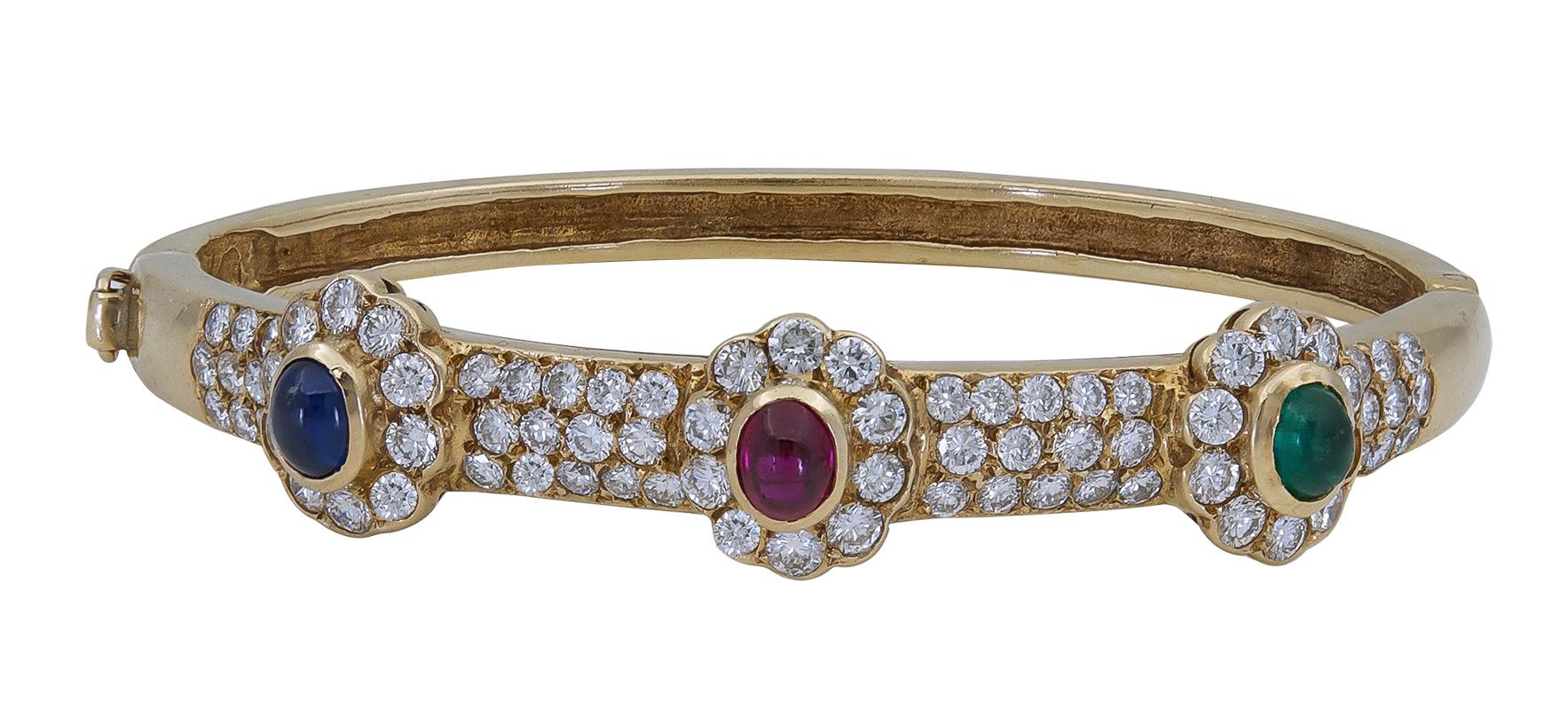 A beautiful bangle bracelet showcasing cabochon shaped ruby, sapphire, and emerald, surrounded by brilliant diamond petals. Each flower is spaced by round diamonds set in yellow gold. 
Fits up to a 6 inch wrist.
Up to 2 cm in thickness.