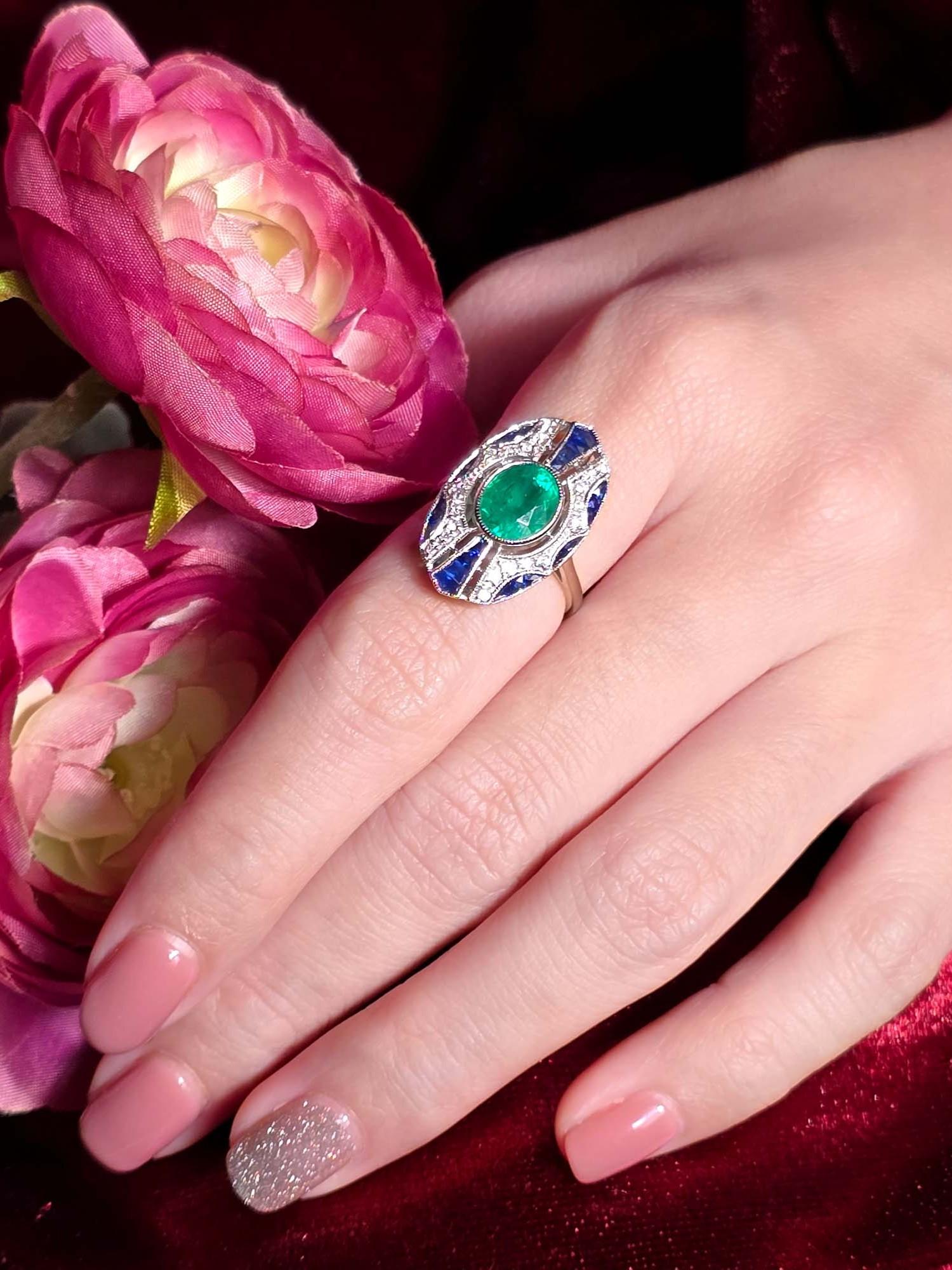 Faites une déclaration audacieuse avec cette bague de style Art déco, ornée d'une émeraude ovale au centre. Entouré de diamants étincelants et délicatement rehaussé de saphirs d'un bleu profond. Le design allie la richesse des couleurs et l'élégance