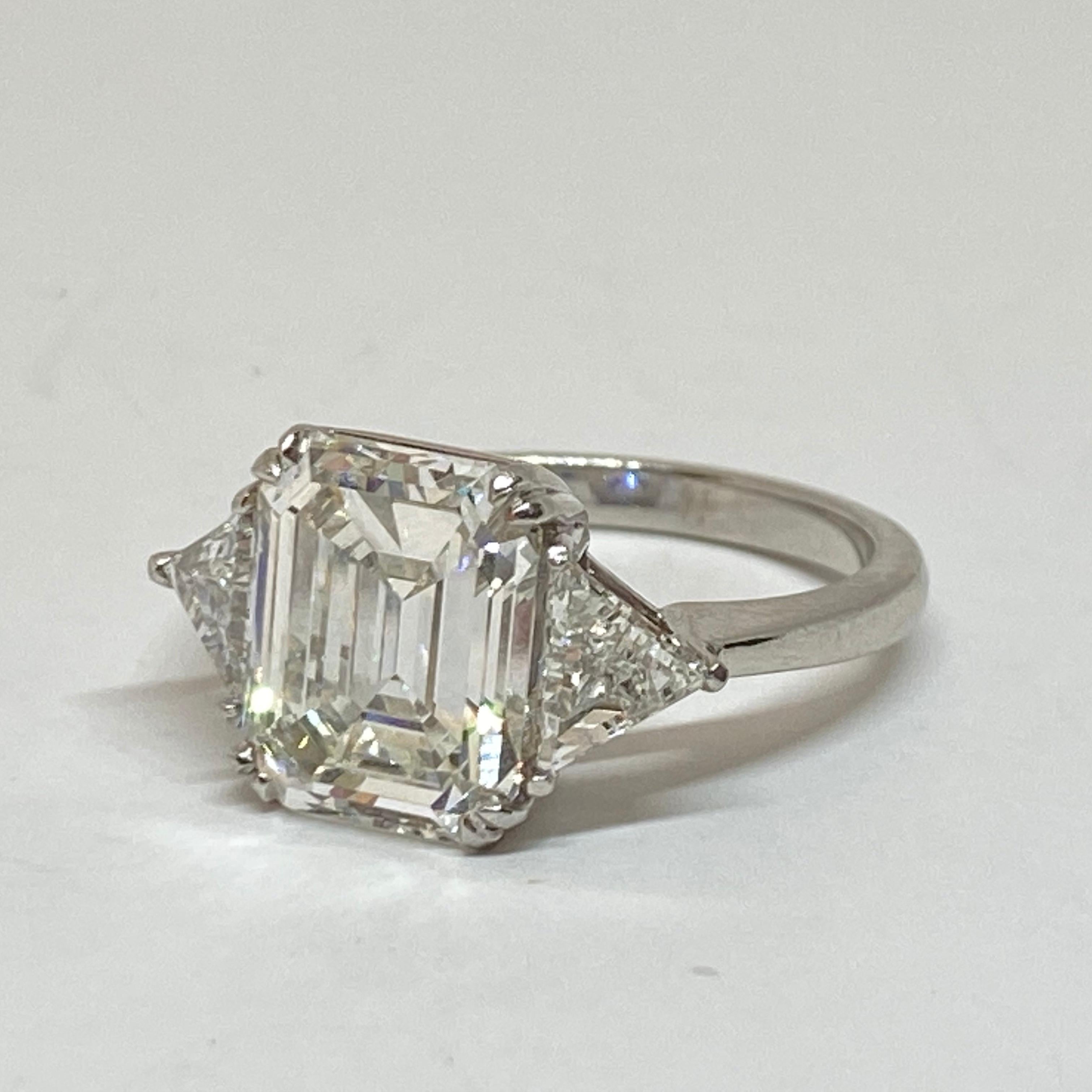 Beautiful three stone engagement ring designed in platinum and set with a stunning emerald cut diamond center and two trillian cut side diamonds that total .69 carats. Classic three stone ring can be sized upon request for any finger size. Comes