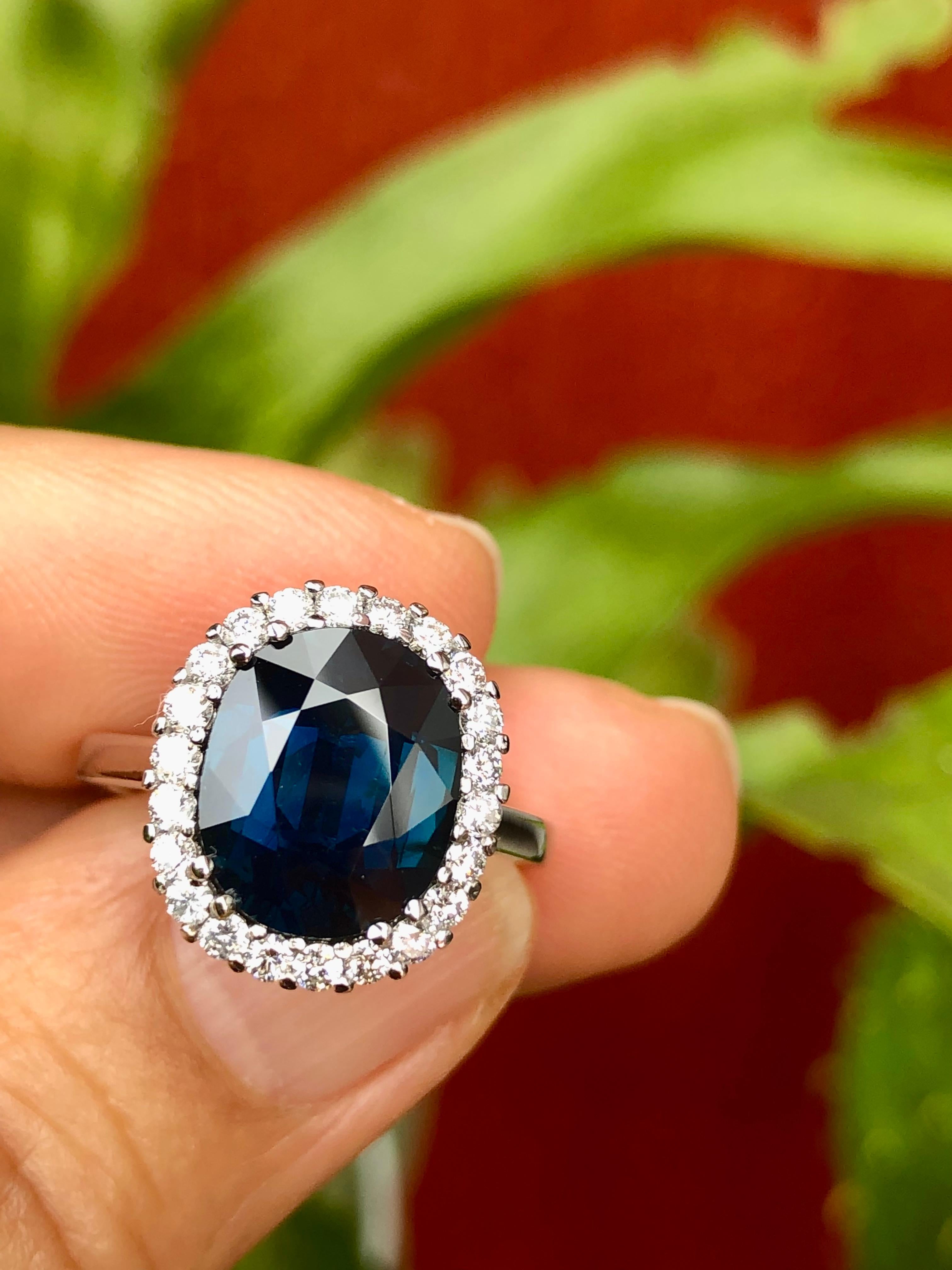 A beautiful oval cut no heat natural sapphire diamond halo engagement ring set in 18k white gold. The ring design highlights an oval-cut 5.31 carat no heat sapphire midnight blue color. This sapphire is then haloed by round brilliant cut diamonds