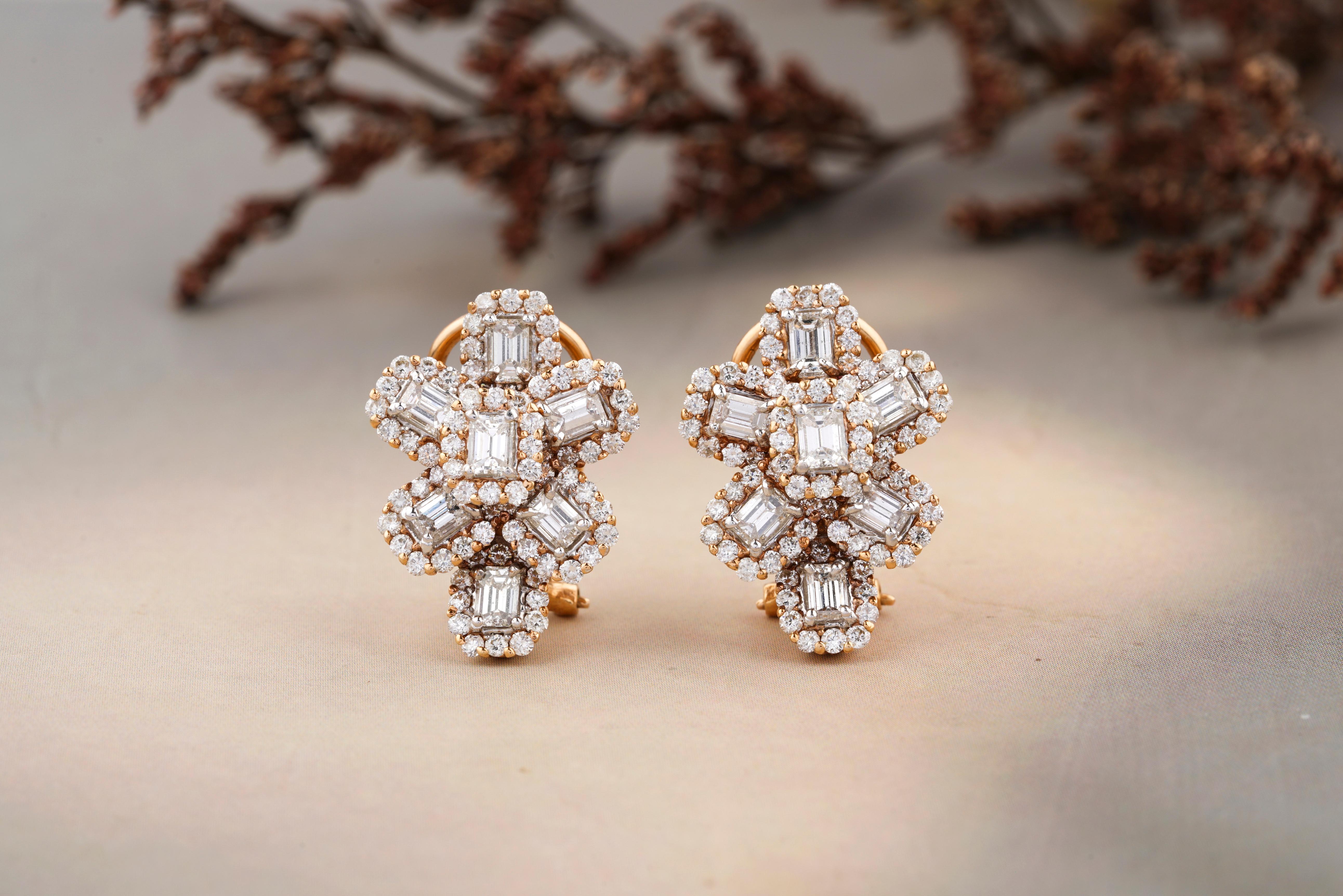 These earrings feature a stunning floral design with a combination of emerald cut and round cut diamonds set in 18k gold. The round cut diamonds create an outline around the center emerald cut diamonds, giving the earrings a unique and eye-catching