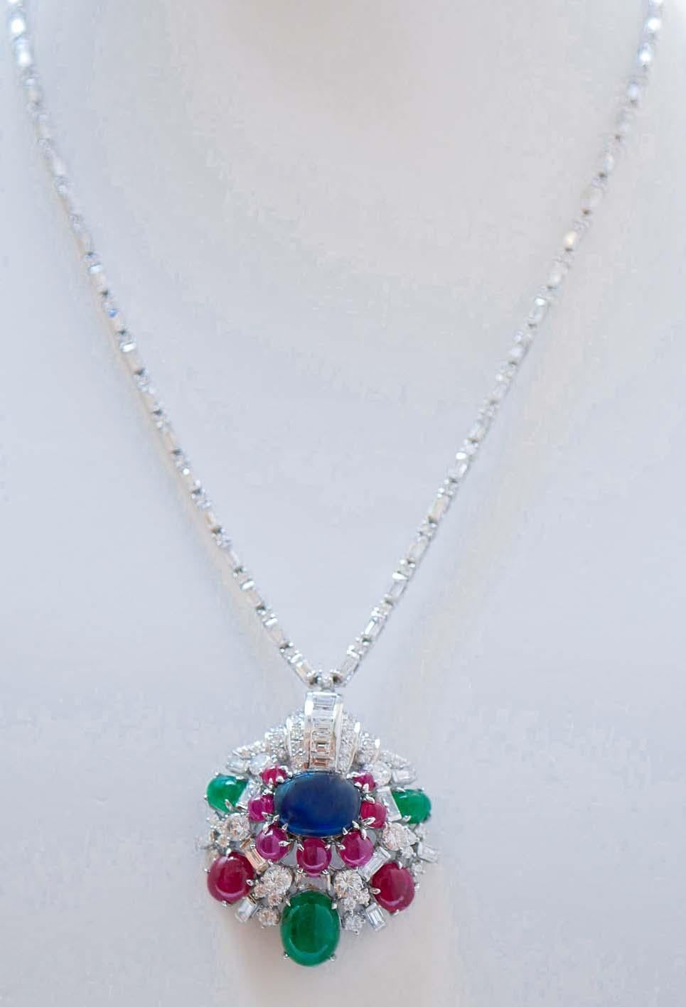 Elegante collar colgante de estructura de oro blanco de 18 kt montado con un zafiro central rodeado de rubíes, diamantes y esmeraldas. A lo largo de la cadena,  diamantes. El colgante se puede quitar para llevar sólo el collar.
Este collar colgante