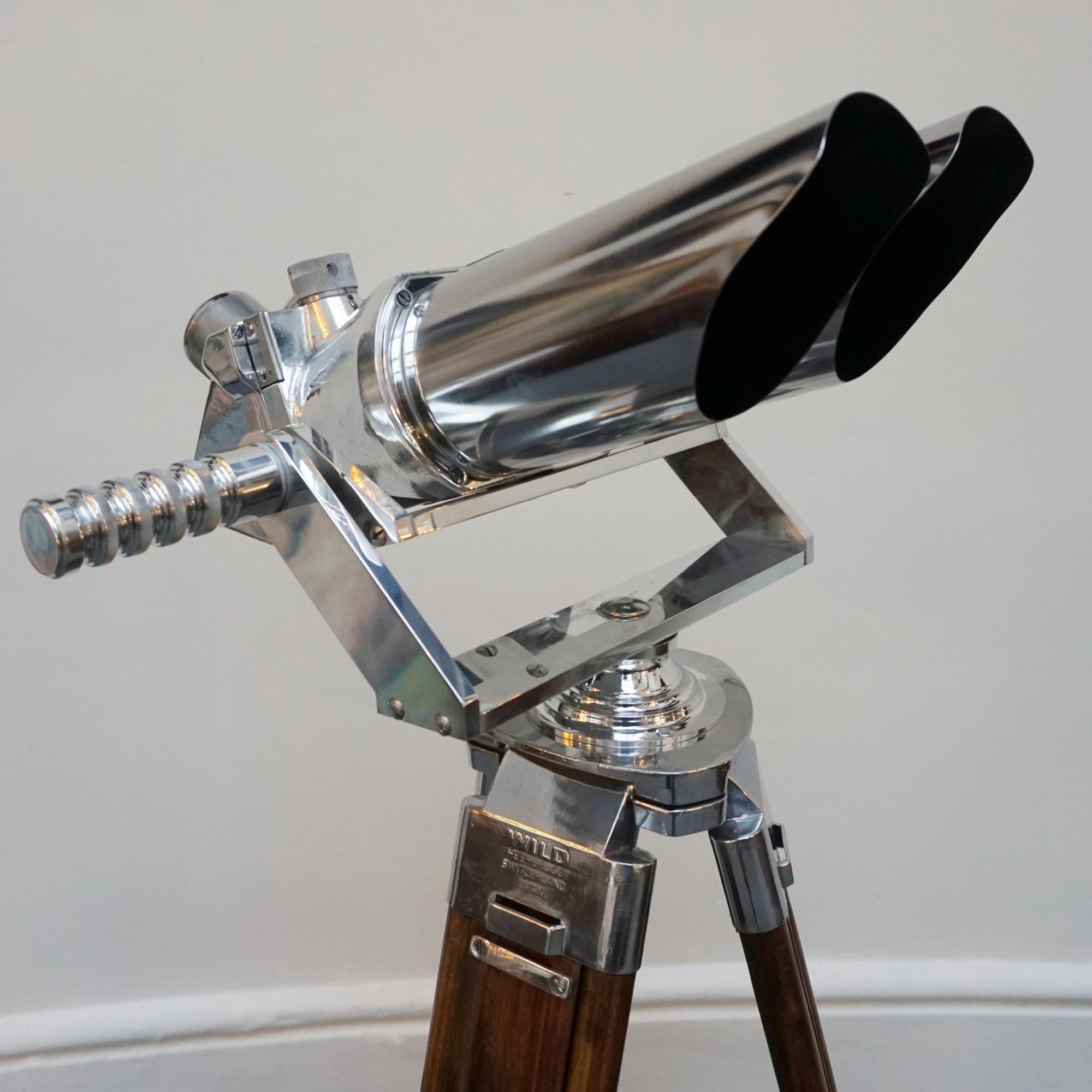 A pair of 10x80 observation binoculars designed by Emil Busch Optical Industries of Rathenow. WW11 naval binoculars with eyepieces set at 45 degrees. Set on a later extending wood and chromed metal stand, with chromed conical feet. This design was