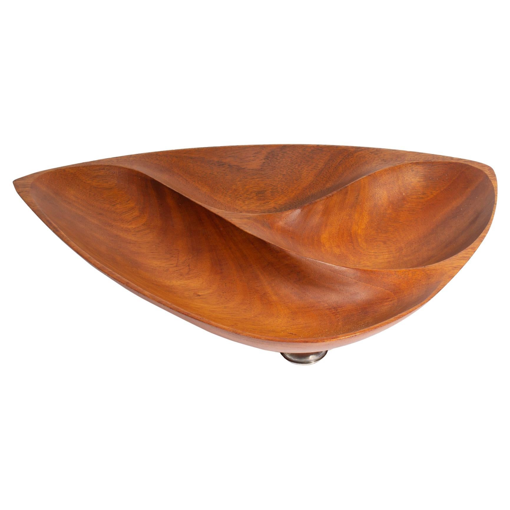 A divided console bowl carved by American woodworker Emil Milan (1922-1985). Carved from African mahogany, also known as Khaya wood, the bowl is divided into three parts and stands on three weighted sterling silver feet below. The underside of the