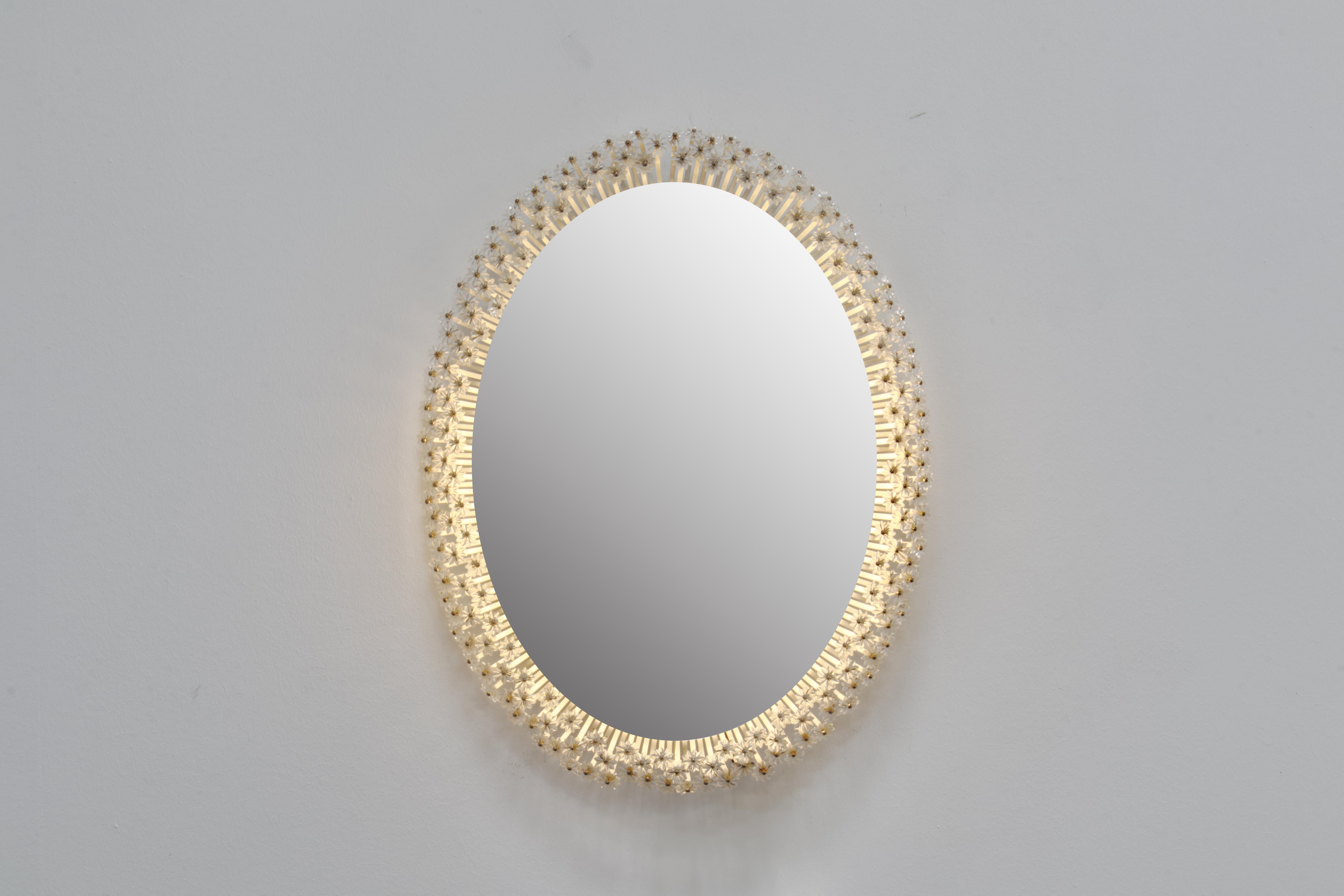 Stunningly beautiful backlit oval wall mirror with a halo of over 200 crystals dispersing the light extraordinarily. Designed and made in 1950s Austria by Emil Steiner and Rupert Nikoll respectively.

The piece is constructed of an oval steel plate,