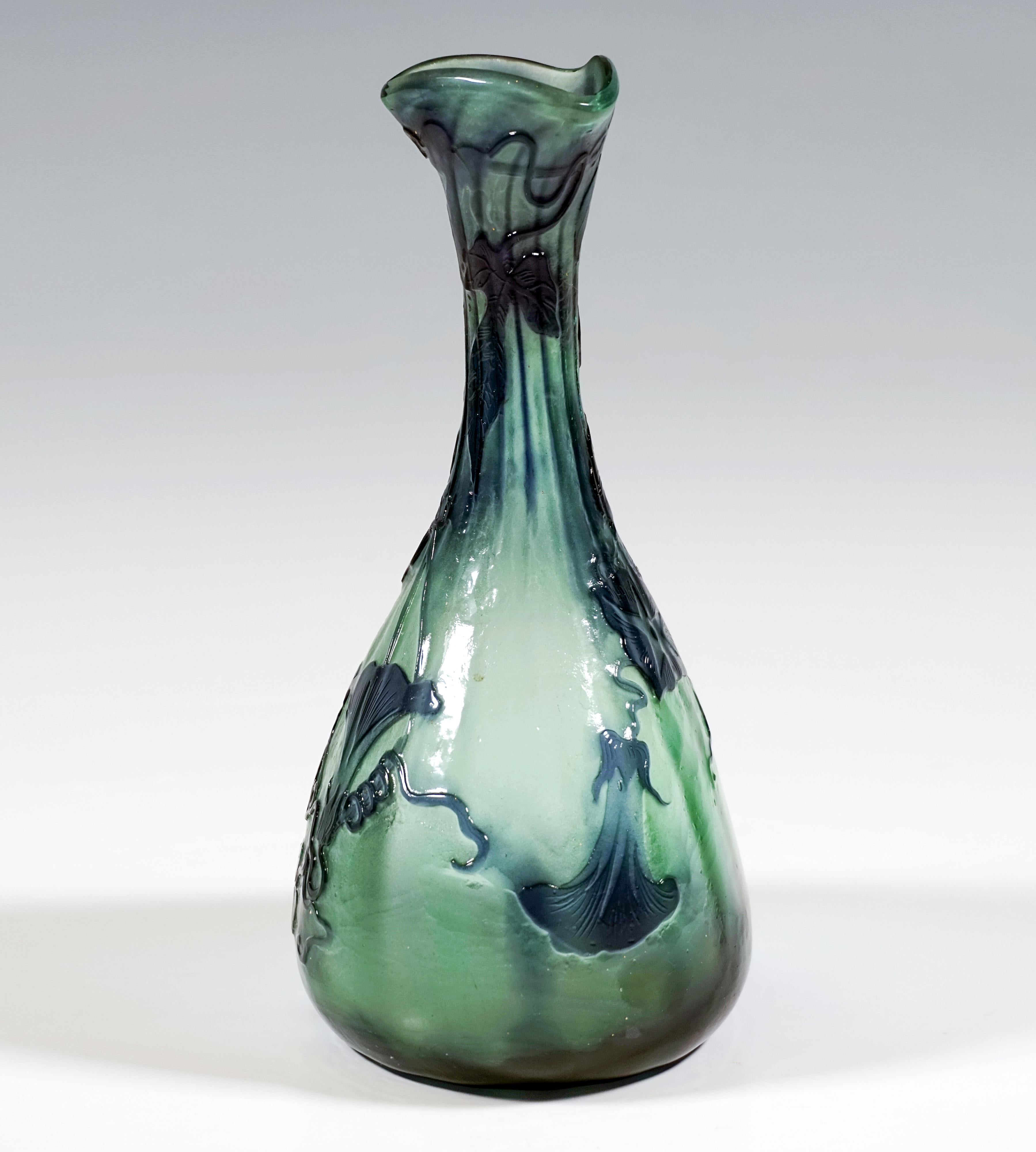 Vase optiquement soufflé à corps bulbeux et long col élancé, base ronde, corps de section ovale, bouche évasée pincée en forme de trèfle, verre vert menthe avec inclusions de poudre fondue bleu foncé au fond et sur le col, 16 facettes et encoche sur