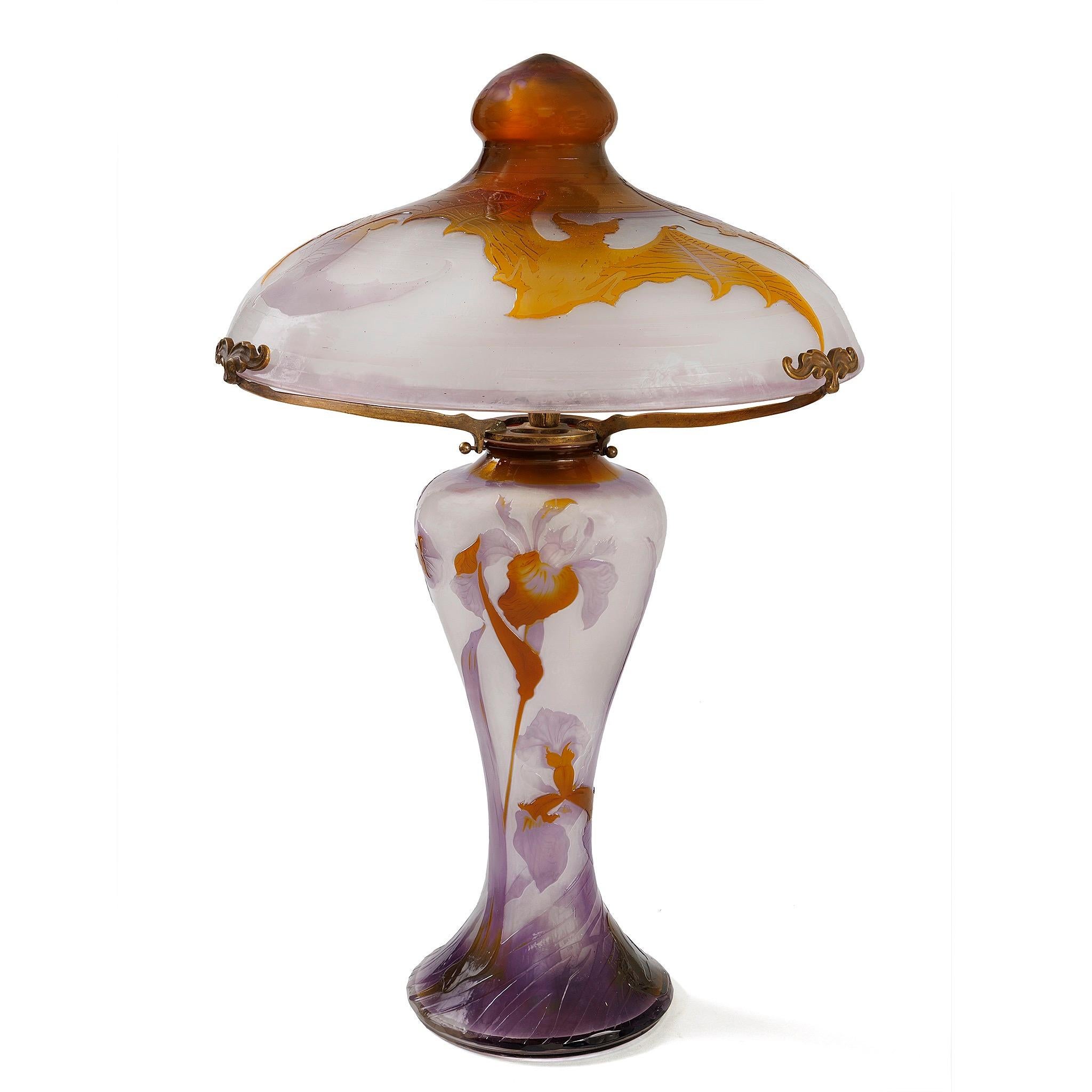 Cette exquise lampe chauve-souris Galle est fabriquée en verre camaïeu de trois couleurs, avec un abat-jour délicat de couleur lavande orné d'un fleuron doré, maintenu par trois bras en bronze avec des fleurons floraux. La base est décorée d'une