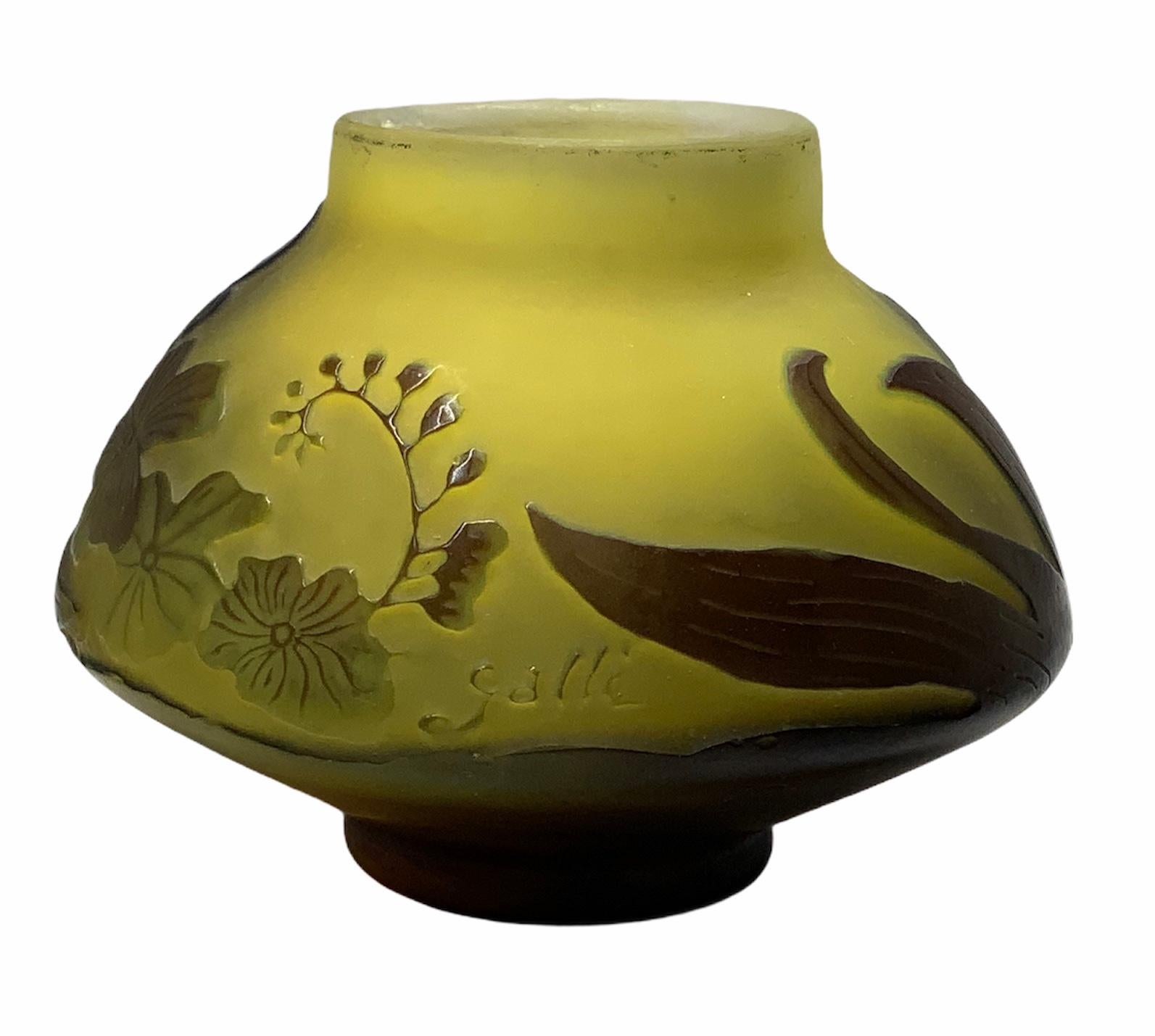 This is a Galle small wide mushroom shaped vase. It has a frosted yellow glass background highlighted by wine color branches of violets flowers & leaves. The wine color covers completely the base. The glass is signed Galle.