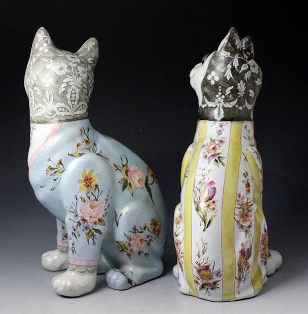 Dated: circa 1900 Nancy France

A pair of pottery Emile Galle pottery faience glaze comical cat with green glass eyes. 
The felines are decorated wearing a chintz outfit with black lace caps. 
Both cats have lockets with images of their unlikely
