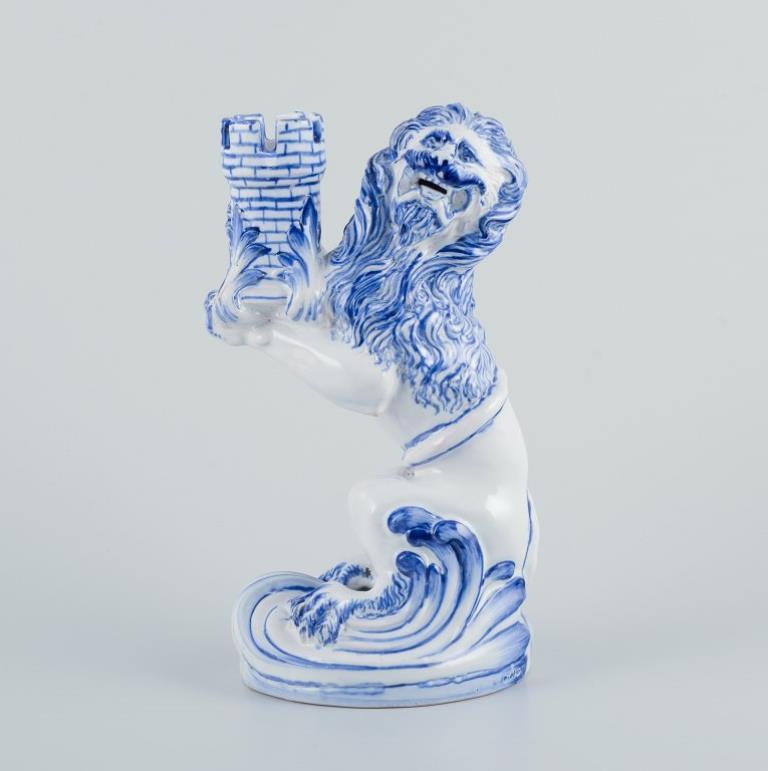 Emile Gallé for Nancy, St Clement. 
A pair of early and large blue and white faience candle holders modelled as a seated roaring lion with its tail wrapped around its body, presenting a turret enclosed by foliage with its front paws, on an oval