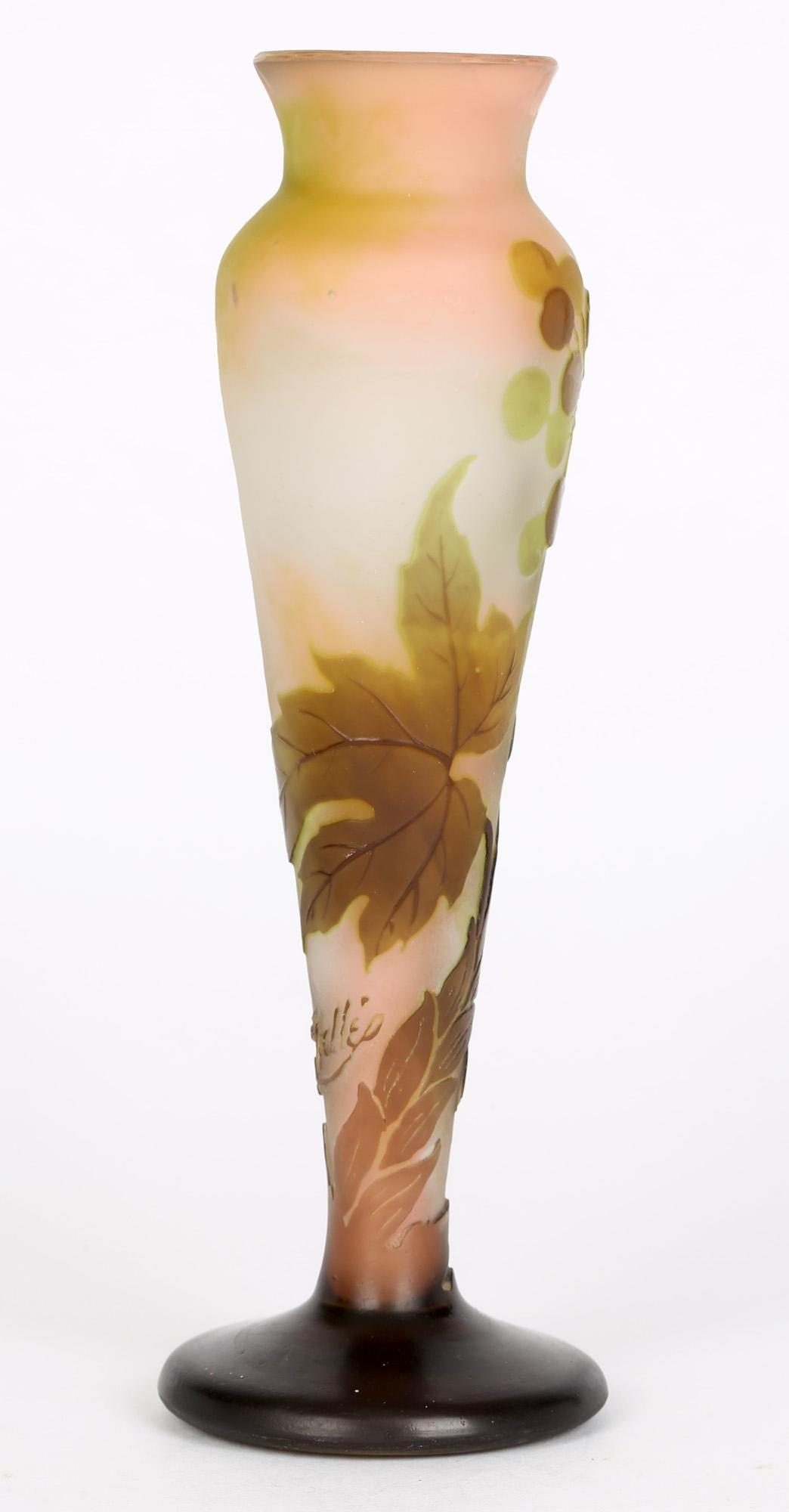 A fine and stylish French cameo and cased tall glass vase decorated with seed pods on tall scrolling leafy stems made by Emile Galle and dating from around 1905. The vase is made in pink, green and brown colors and is overlaid and acid etched with