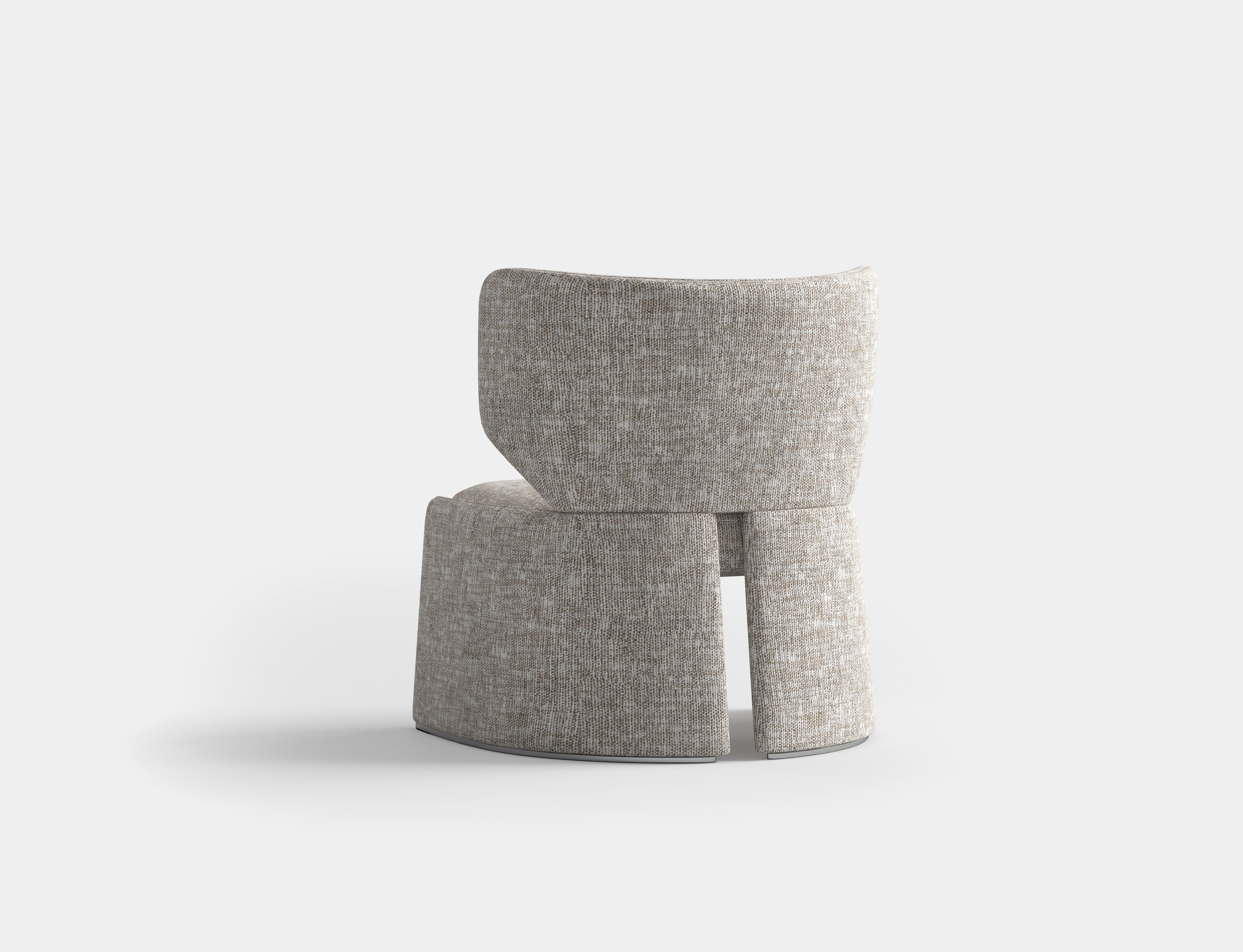 Ce fauteuil a  design moderne et minimaliste avec une structure sculpturale et géométrique. Il est doté d'un dossier large et légèrement incurvé et d'une assise épaisse et rembourrée, tous deux revêtus de tissu ou de cuir. Les pieds de la chaise se