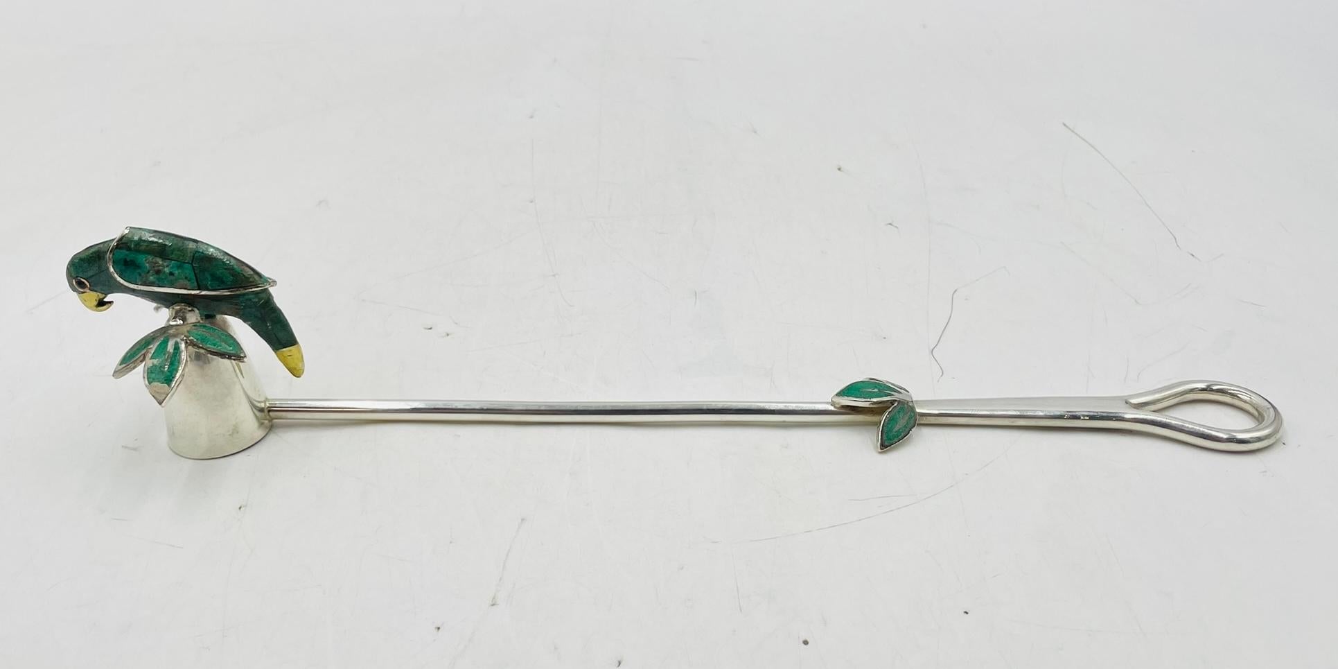 An exquisite candle snuffer designed by acclaimed Mexican artist Emilia Castillo, handcrafted in silver plate with intricate accents of crushed emerald, malachite, and brass. The handle ends in a delicate loop, while the snuffer itself is adorned