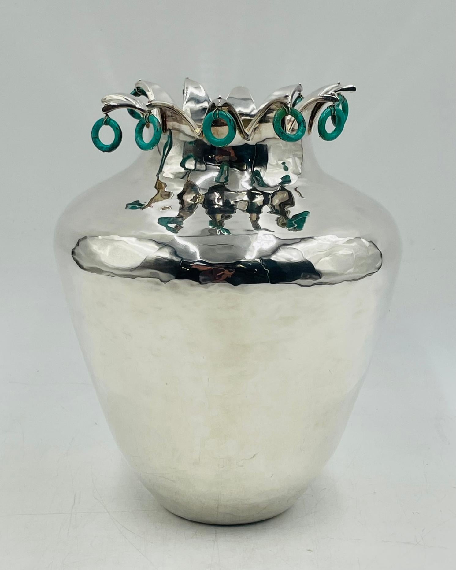 Un bellissimo vaso in argento martellato a mano di Emilia Castillo, arricchito da un bordo a forma di corona ornato da anelli di pietra naturale penzolanti. La superficie scintillante d'argento contrasta elegantemente con le vibranti tonalità verdi