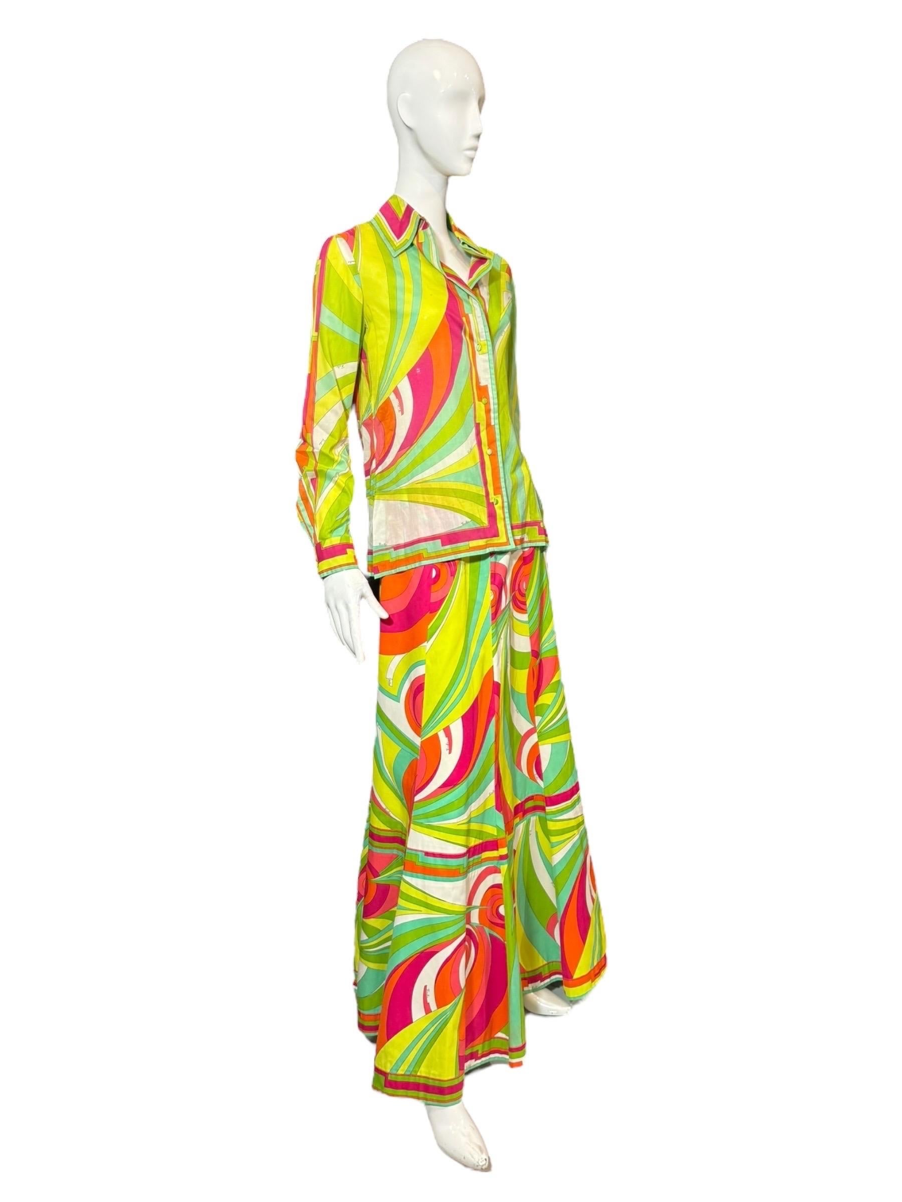 An iconic example of Emilio Pucci’s psychedelic glamour, this original 1970s blouse and maxi skirt set features the house’s signature swirling geometric print in vibrant hues of lime green, citrus orange, magenta, red, and turquoise. Both pieces are