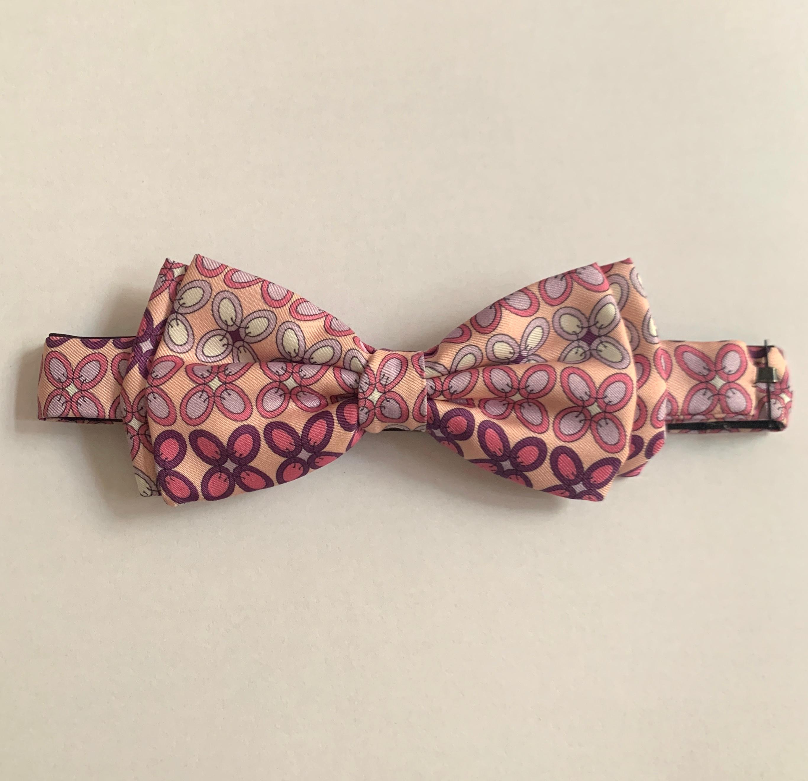 Emilio Pucci pre-tied adjustable pink and purple Pucci print bow tie. Pink and purple pattern resembles petals that have been fastened together with stitches. Fastens with hook that attaches beneath shirt collar.

100% silk.

Made in Italy.