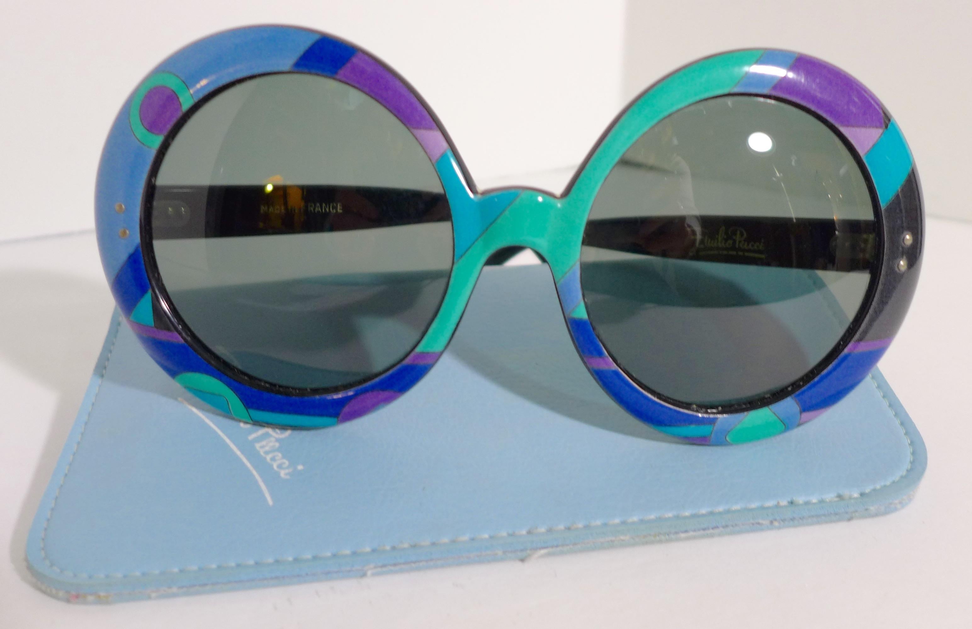 These Emilio Pucci round plastic sunglasses feature a classic blue, green, and purple print. The lenses are black. They come with a baby blue leather case. Made in France. 

Measurements in Inches: 
Width: 6.5 
Height: 3
Length: 5.5