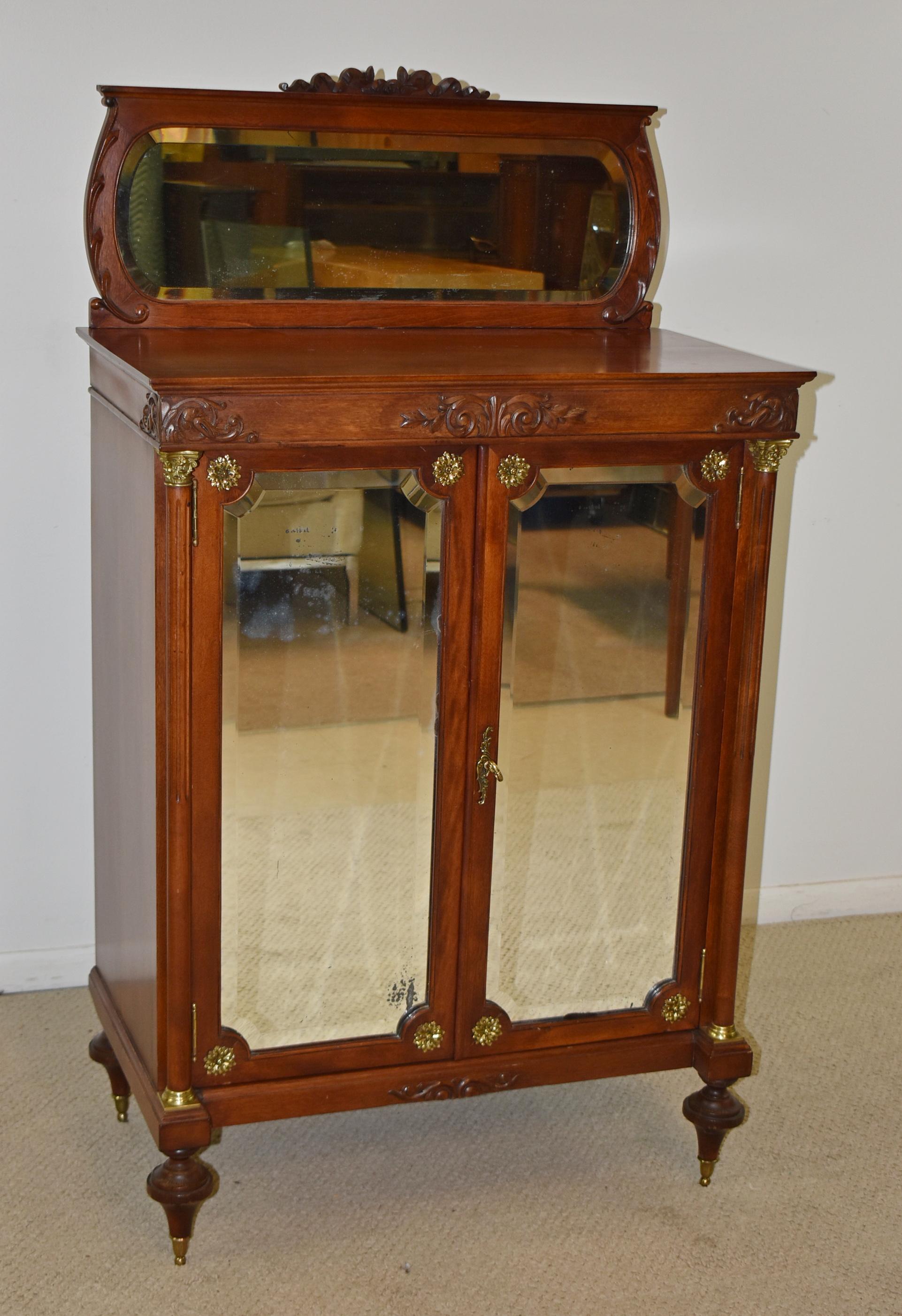 Empire style mahogany music cabinet with two doors and beveled glass mirrors. Brass rosettes in the corners. Fluted pillars have brass mounts. Light finish loss to mirror. Very nice condition. Dimensions: 16.5