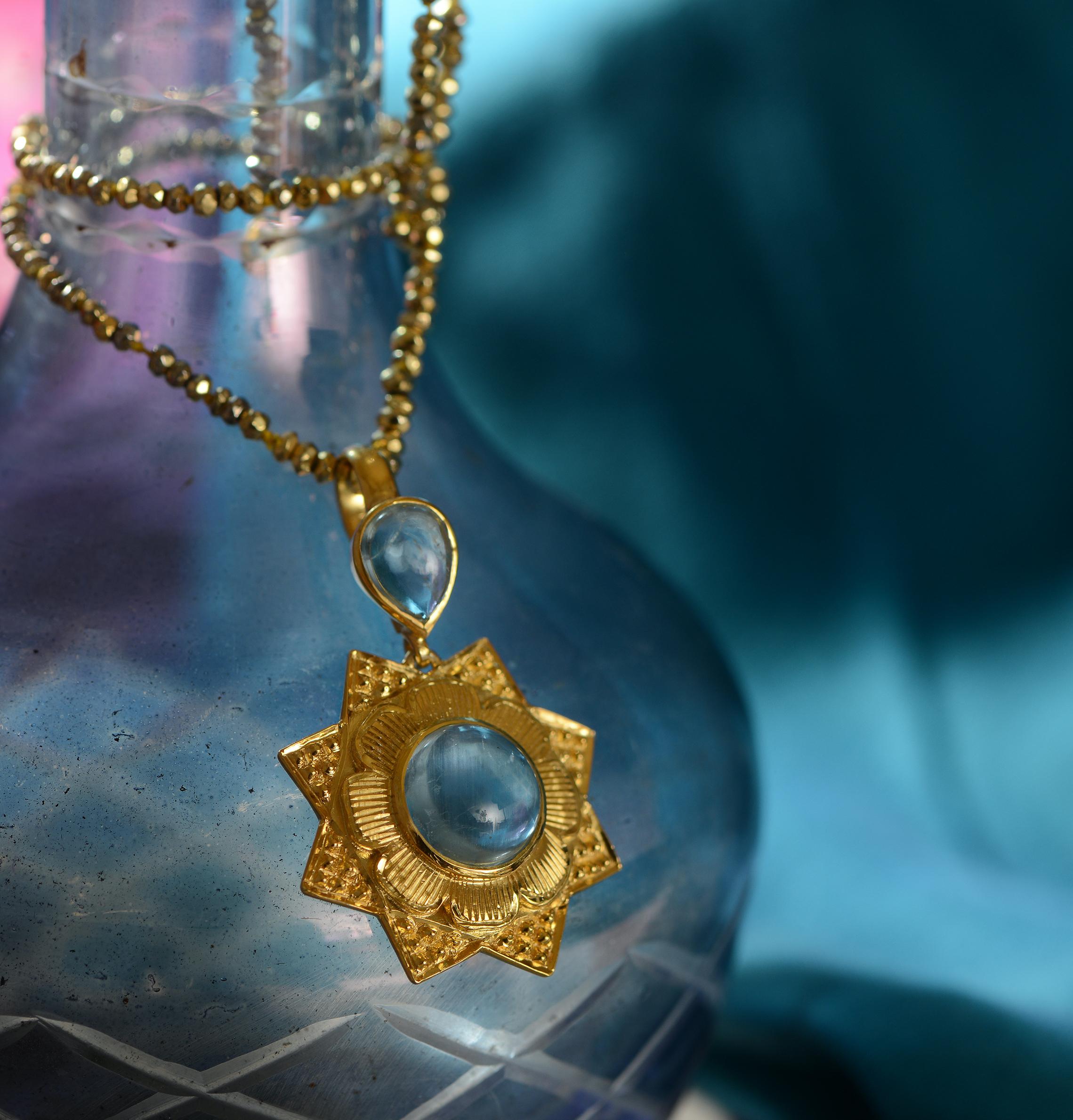 

The Aquamarine Gold Plate Statement Pendant,  is handmade and embedded with cabochon aquamarines. It has been exquisitely hand engraved and has shapes of the sun and stars. The central aquamarine is surrounded by flower petals. It comes with a 20