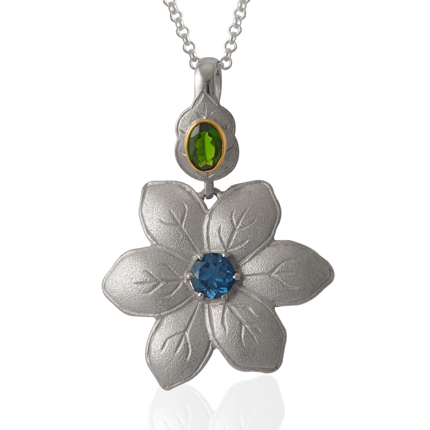 This lovely Blue Topaz Chrome Diopside 18 Karat Gold Silver Flower Pendant, has been handmade in our workshops. It is made of frosted sterling silver and has hand engraved petals. The central stone is a london blue topaz and the pendant is capped