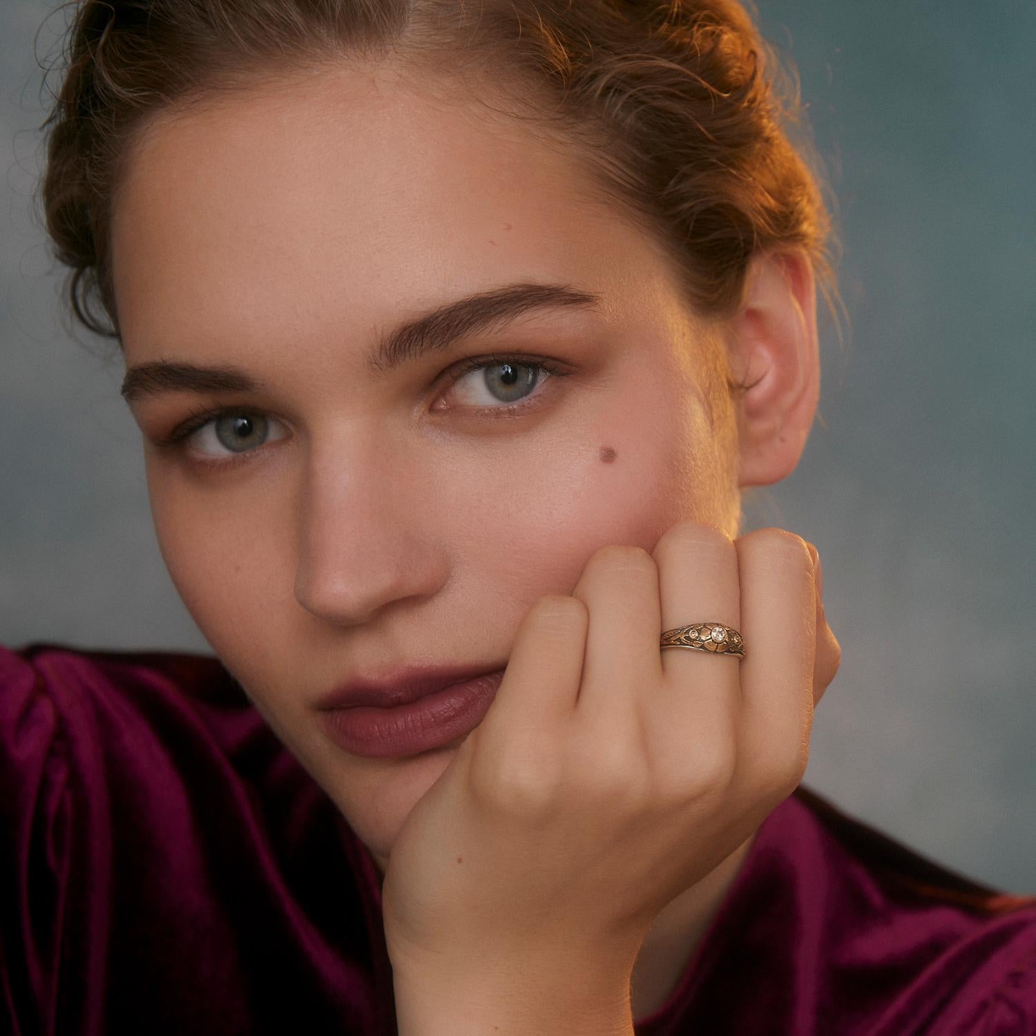 Cette jolie bague de fiançailles en or et diamant est unique en son genre. Fabriquée à la main dans nos ateliers, elle présente un diamant central pleine taille, flanqué de deux autres diamants pleine taille, tous sertis dans des motifs floraux