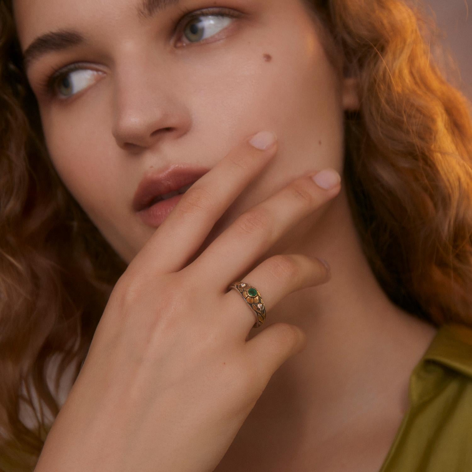Cette adorable bague en émeraude et diamant est unique en son genre. Fabriqué à la main dans nos ateliers, il présente une émeraude centrale flanquée de deux diamants pleine taille, le tout serti dans des motifs de fleurs et de feuilles en or jaune