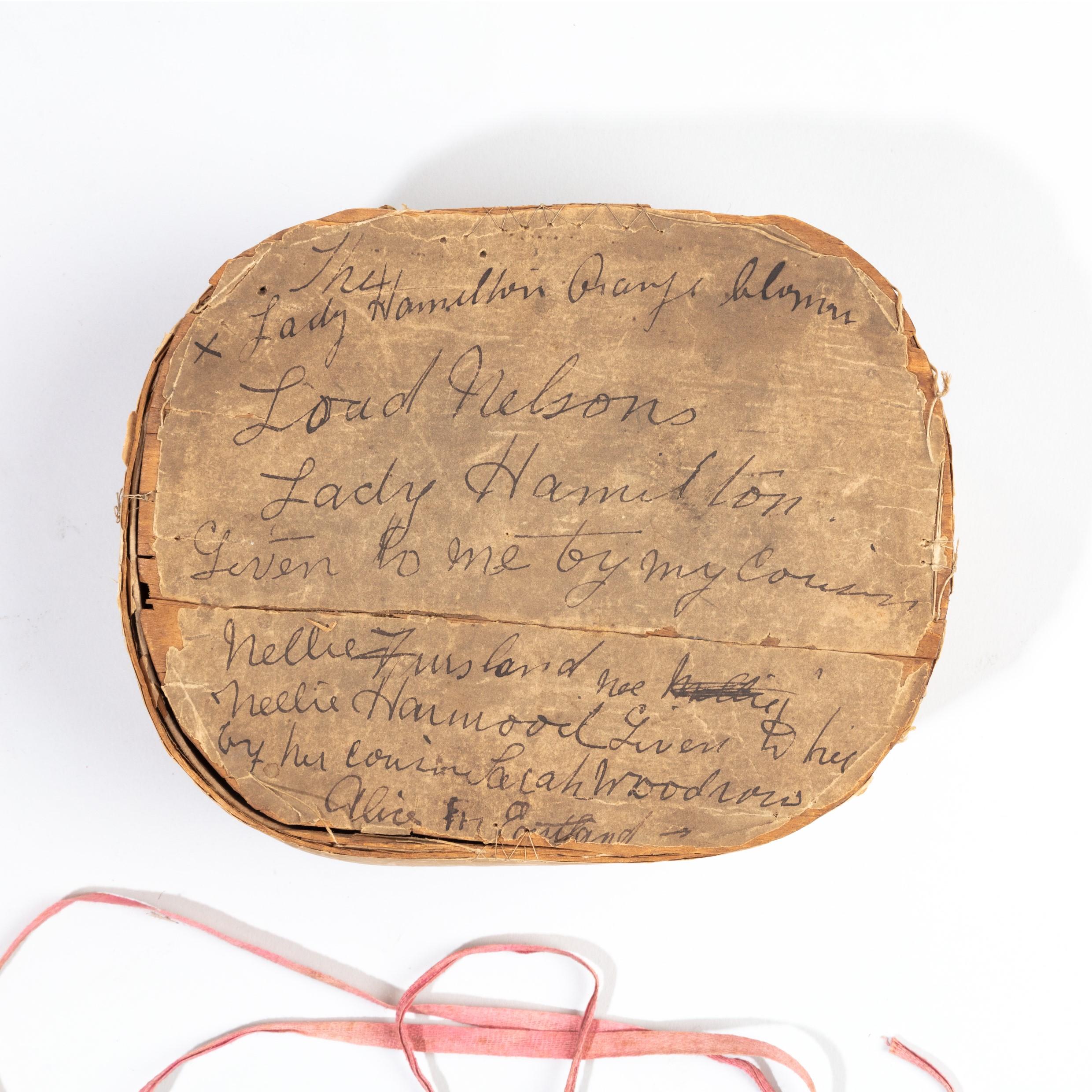 This charming keepsake comprises an oval paper lined wooden box and lid, formally a pill or pantry box, held together with a pink ribbon, inscribed on the lid The Lady Hamilton’s Orange blossom. Lord Nelsons. Lady Hamilton. Given to me by my cousin