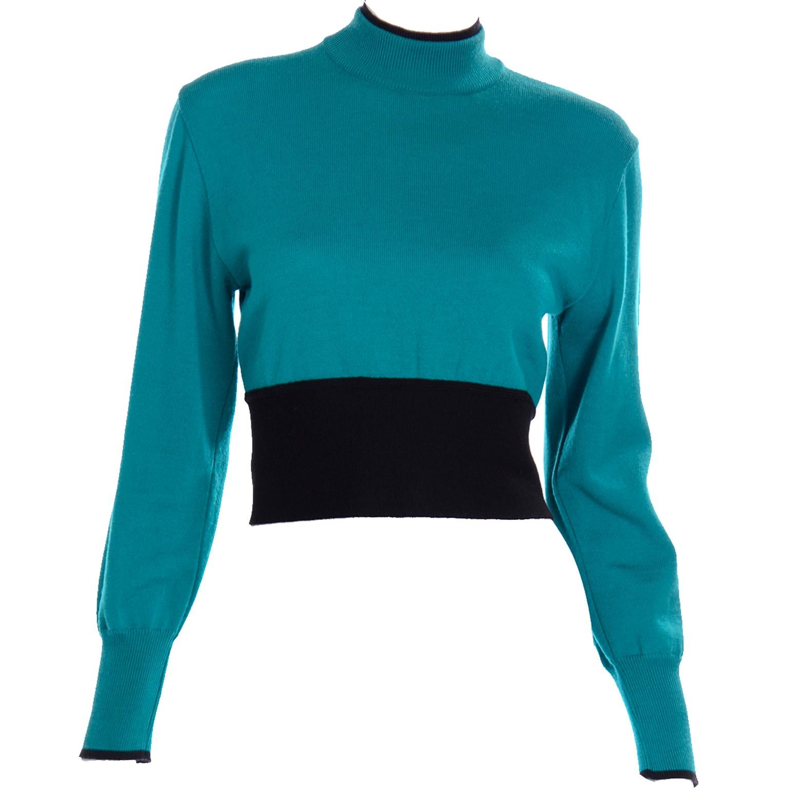 This vintage Emmanuelle Khanh teal wool sweater has a beautiful navy blue sash. The collar of the sweater top is a mock neck and has two layers, one being navy blue and the other teal. The sleeves are long and have a small navy blue tip at the