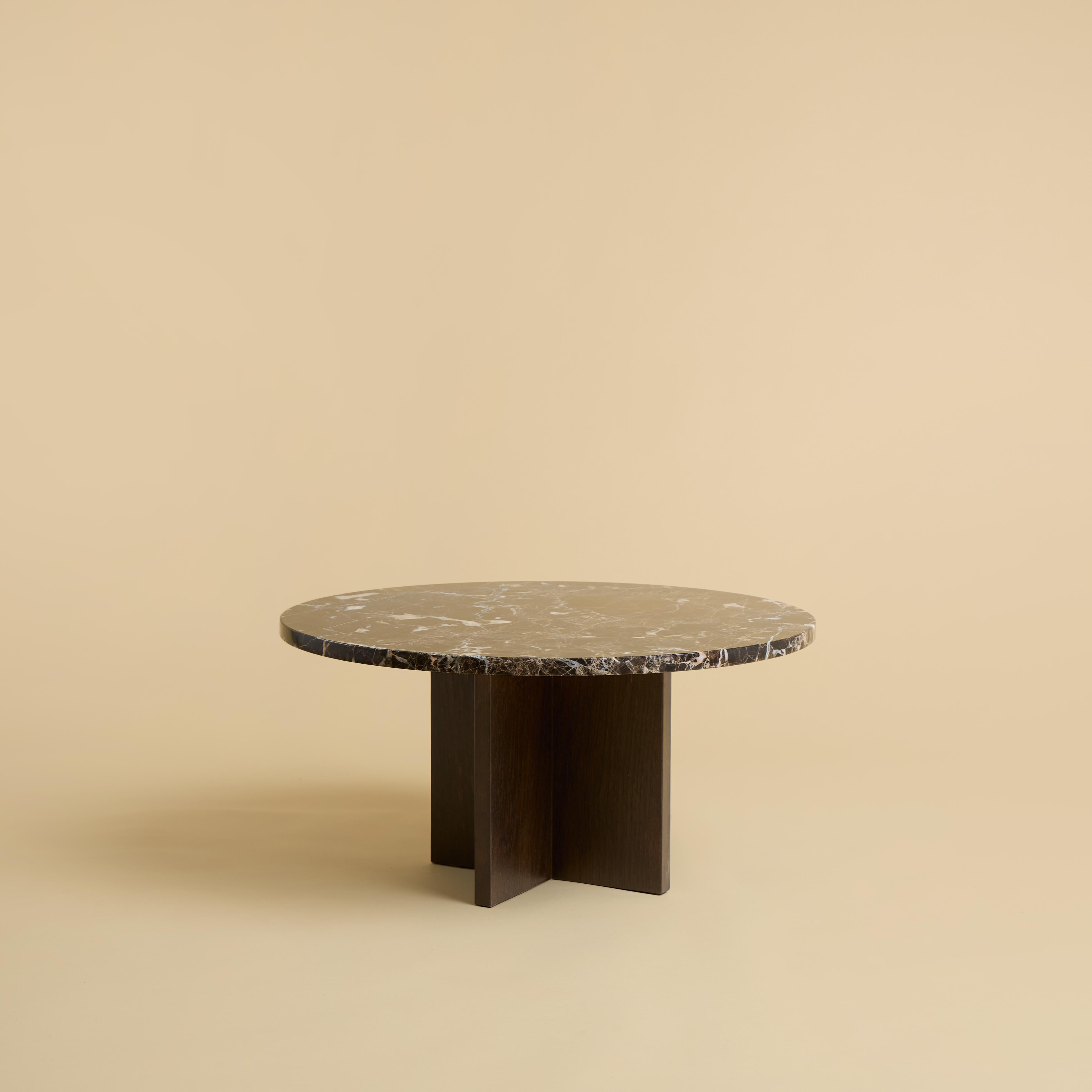 Der Couchtisch Tinian wird mit einem Untergestell aus Eichenholz und einer Platte aus Marmor Emperador Dark hergestellt. Die Platte ist kreisförmig und hat einen Durchmesser von 60 cm, während der Sockel aus rechtwinklig zueinander verleimten