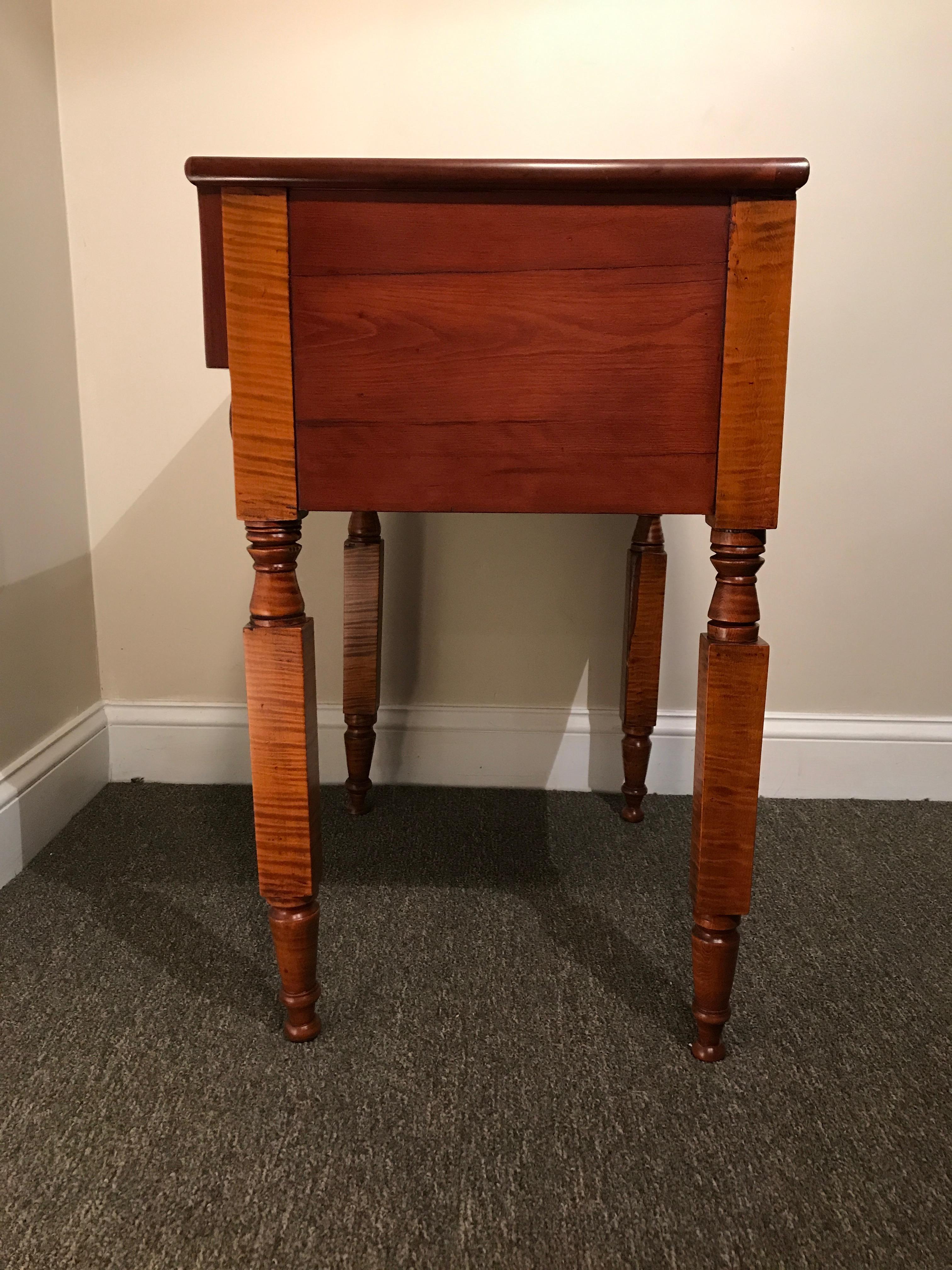 Empire 2-drawer stand in tiger maple, cherry and flamed mahogany, circa 1820. Provenance: Saratoga, NY. Turned legs, dovetailed drawers, top drawer is flamed mahogany, Top front border is veneered with flames mahogany as well, wooden knobs. This