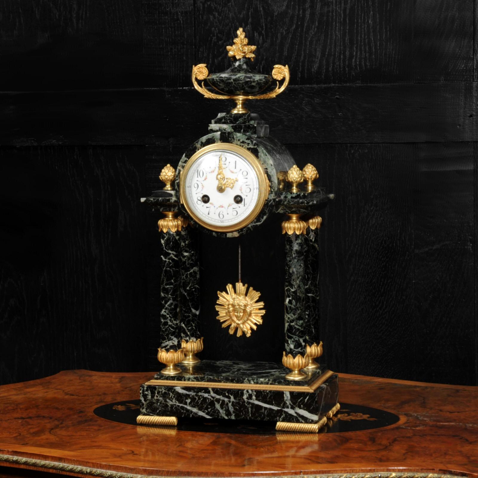 A superb original antique French portico clock. Beautifully modelled in the Empire style in a stunning variegated green marble with finely gilded ormolu bronze mounts. The clock is formed as a four pillar portico, the movement mounted in a drum with