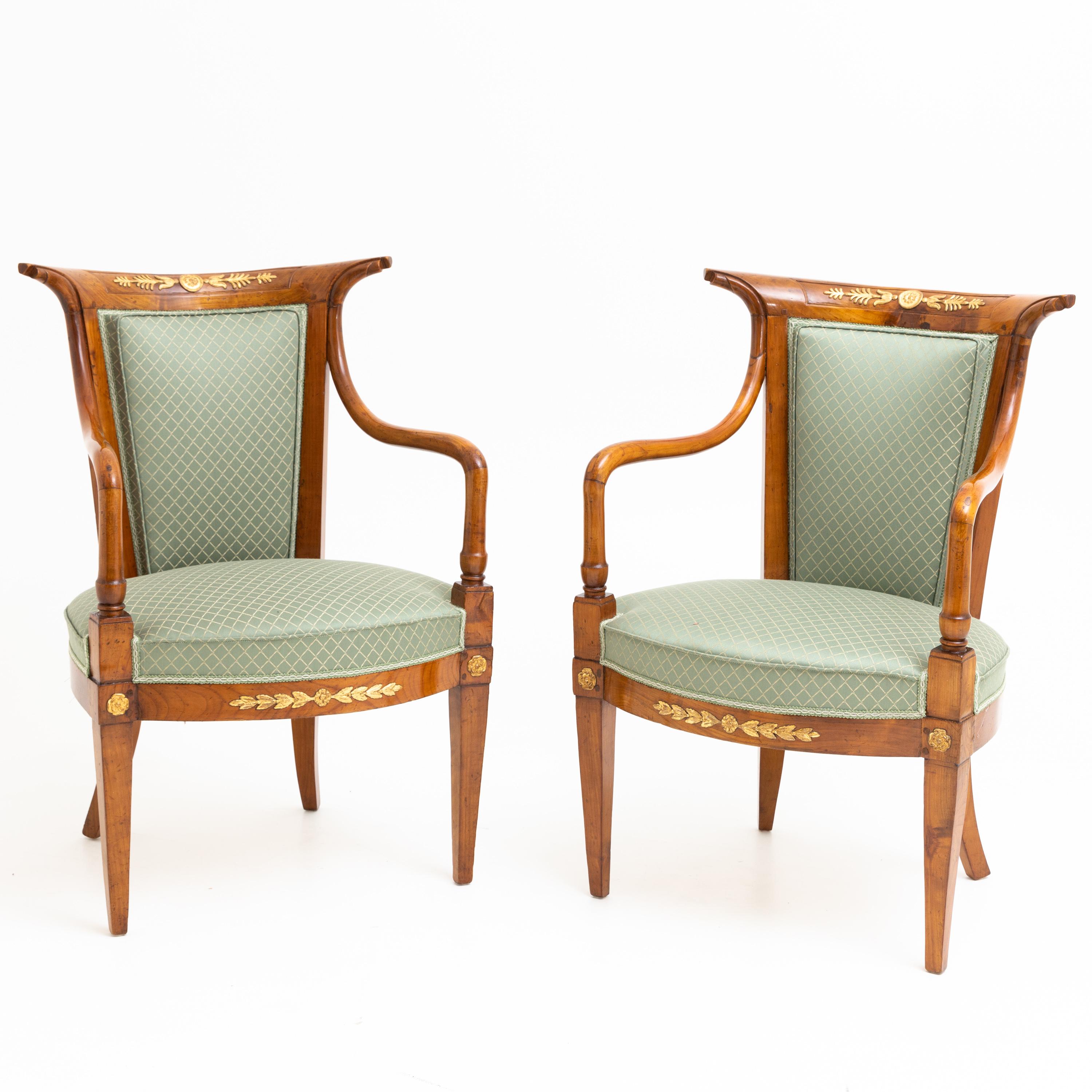 Pair of Italian cherry armchairs with trapezoidal, flared backrests standing on tapered or sabre legs. The elegantly curved armrests lead into the pointed backrests. There and on the frame decorated with stuccoed, gilded leaf and rosette decoration.