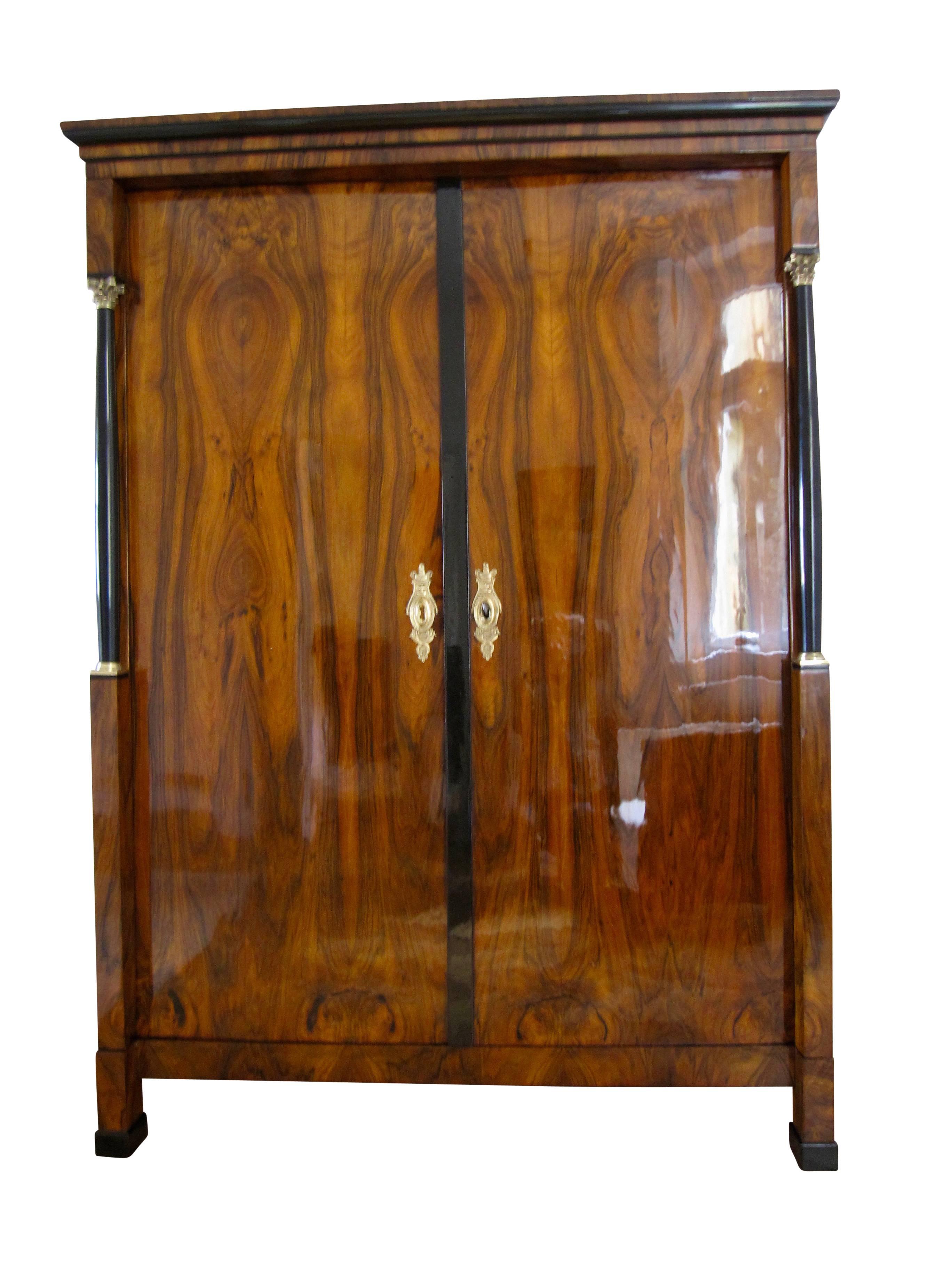 Very elegant Empire / early biedermeier armoire with original brass hardware and lovely walnut veneer. 

It has two ebonized full-columns with brass bases and corinthian capitals. 
The armoire has a beautiful book-matched walnut veneer and is