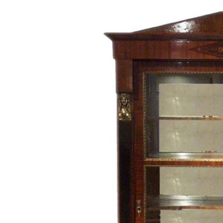Empire bookcase – walnut, rootwood and ebonized wood and columns with brass hardware. Glazed doors with interior shelves above single exterior drawer.