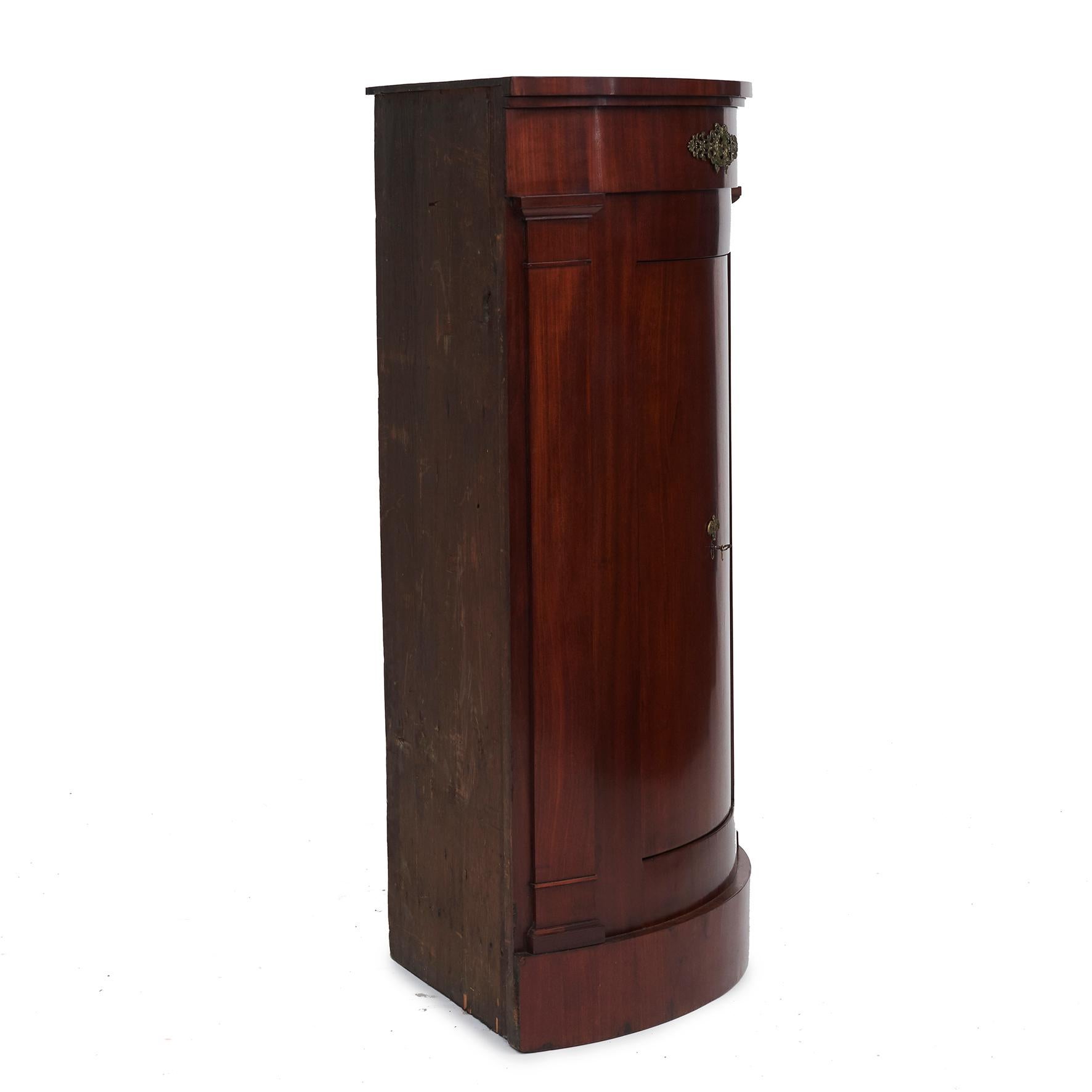 Danish empire bow fronted corner cabinet in flame mahogany.
Bow front with a single door, dressed with brass lock in the middle, flanked by flat coloums with capitals.
Original brass lock and key.
Interior arranged with a trio of useful