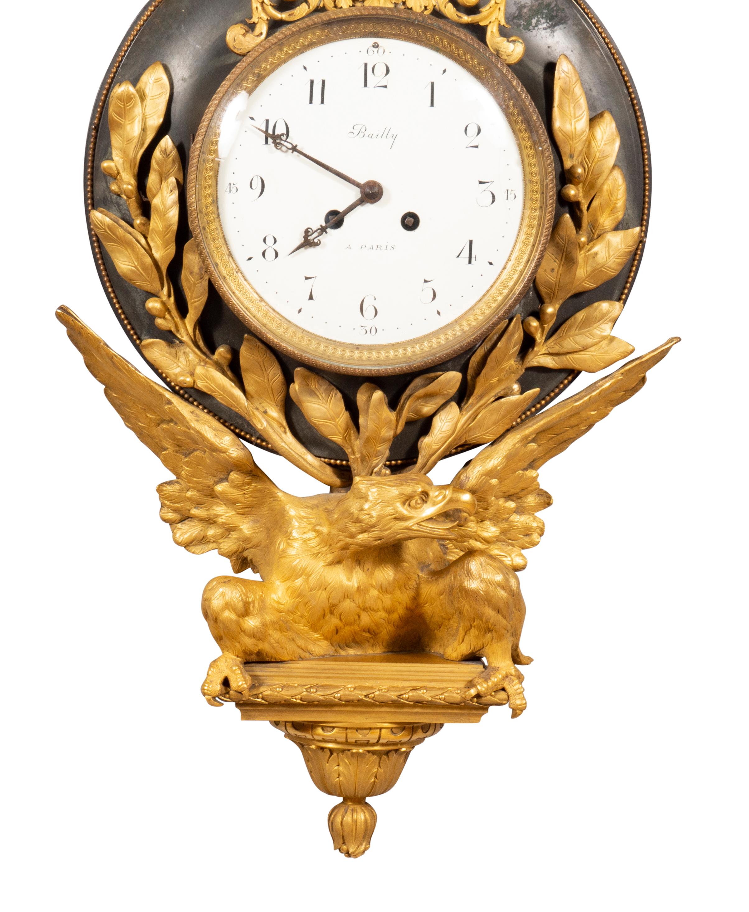 A wall clock with gilt bronze ribbon bow joining a gilt bronze ribbon attached to the clock case with patinated bronze back section and laurel leaf mounted surrounding a circular glass hinged cover opening to an enamelled dial signed Bailly a Paris.