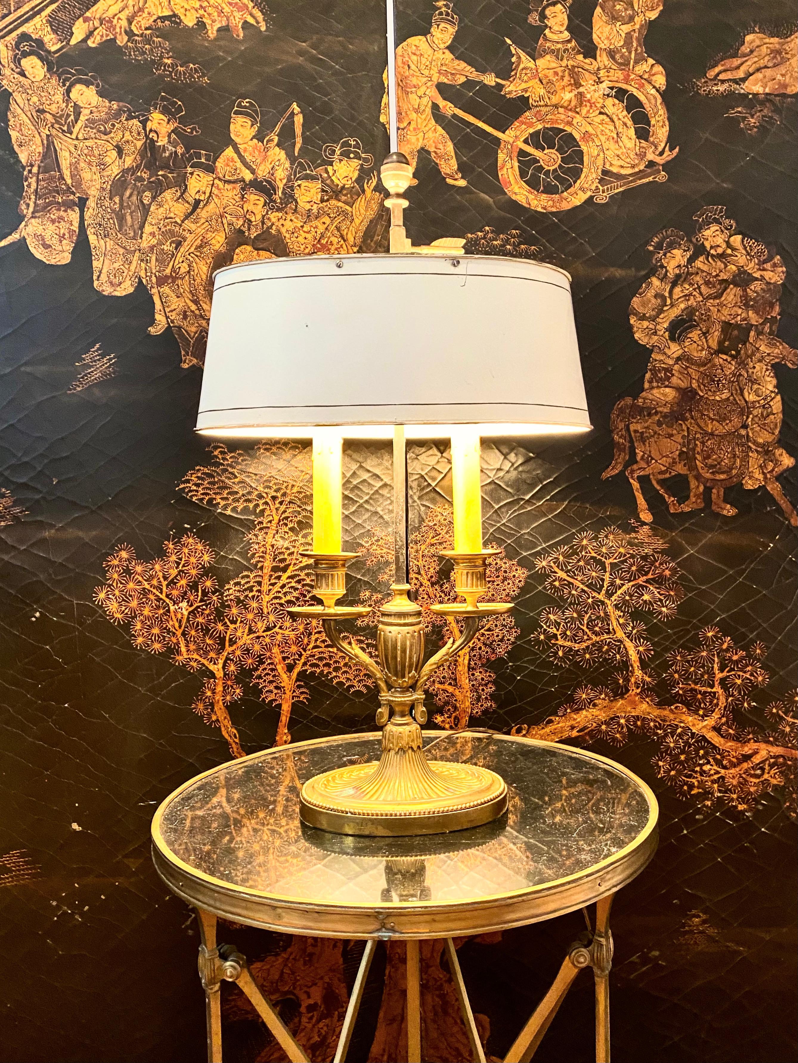 Empire bronze bouillotte lamp, off-white tôle shade.
Empire style bronze 2-arm bouillotte lamp with off-white tôle shade. Classic Empire symbols of the arrow and neo-classical references such as the urn, the pedestal, the acanthus leaves.
Electric