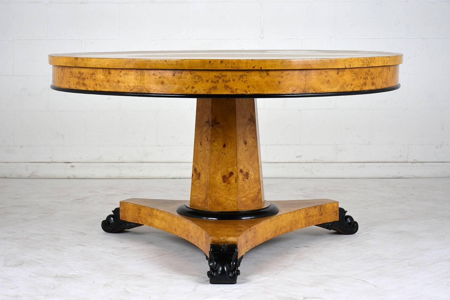 This Vintage French Empire Center Table has been newly restored, is adorned with a burled wood veneers stained a stunning golden color with ebonized details and newly lacquered finish. Accenting the edge of the table and the pedestal are black