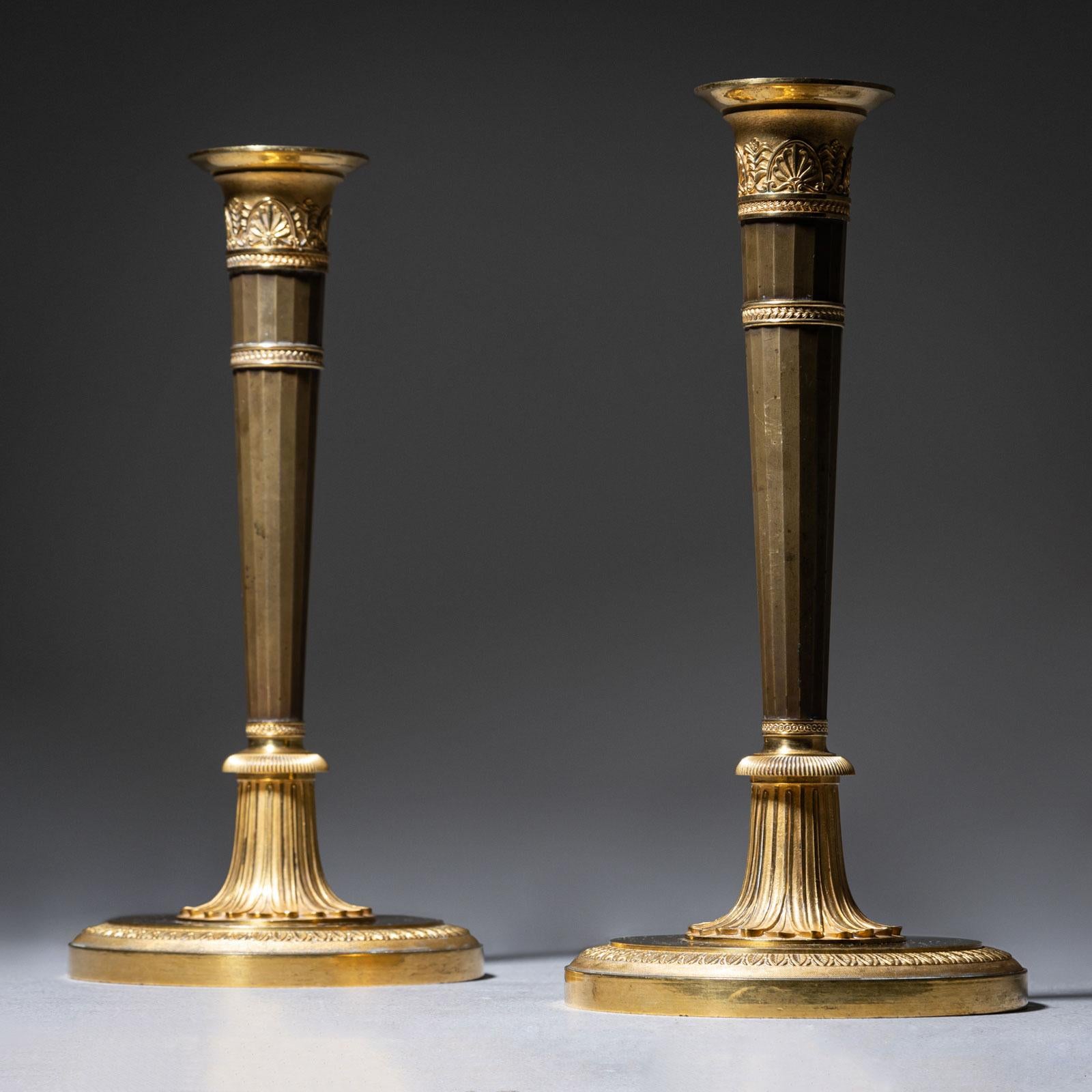 Ein Paar elegante Empire-Kerzenleuchter aus teilweise feuervergoldeter Bronze aus dem frühen 19. Jeder Kerzenhalter steht auf einem runden Sockel mit einem konisch zulaufenden, kannelierten Schaft und einer fein ausgearbeiteten Kerzenfassung.
Die
