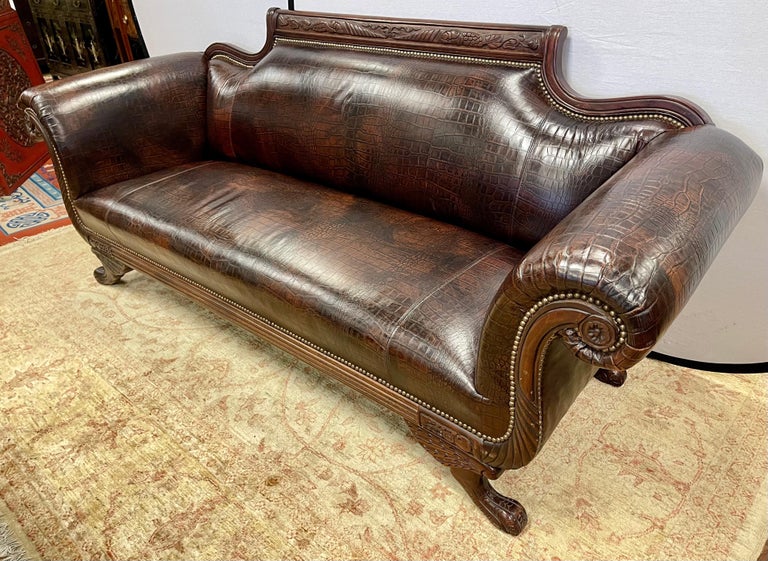 A stunning, totally refurbished Empire sofa with scrolled arms and intricate carvings throughout the mahogany frame including the paw feet. The settee has been updated with a luxurious faux alligator embossed leather upholstery and finished with