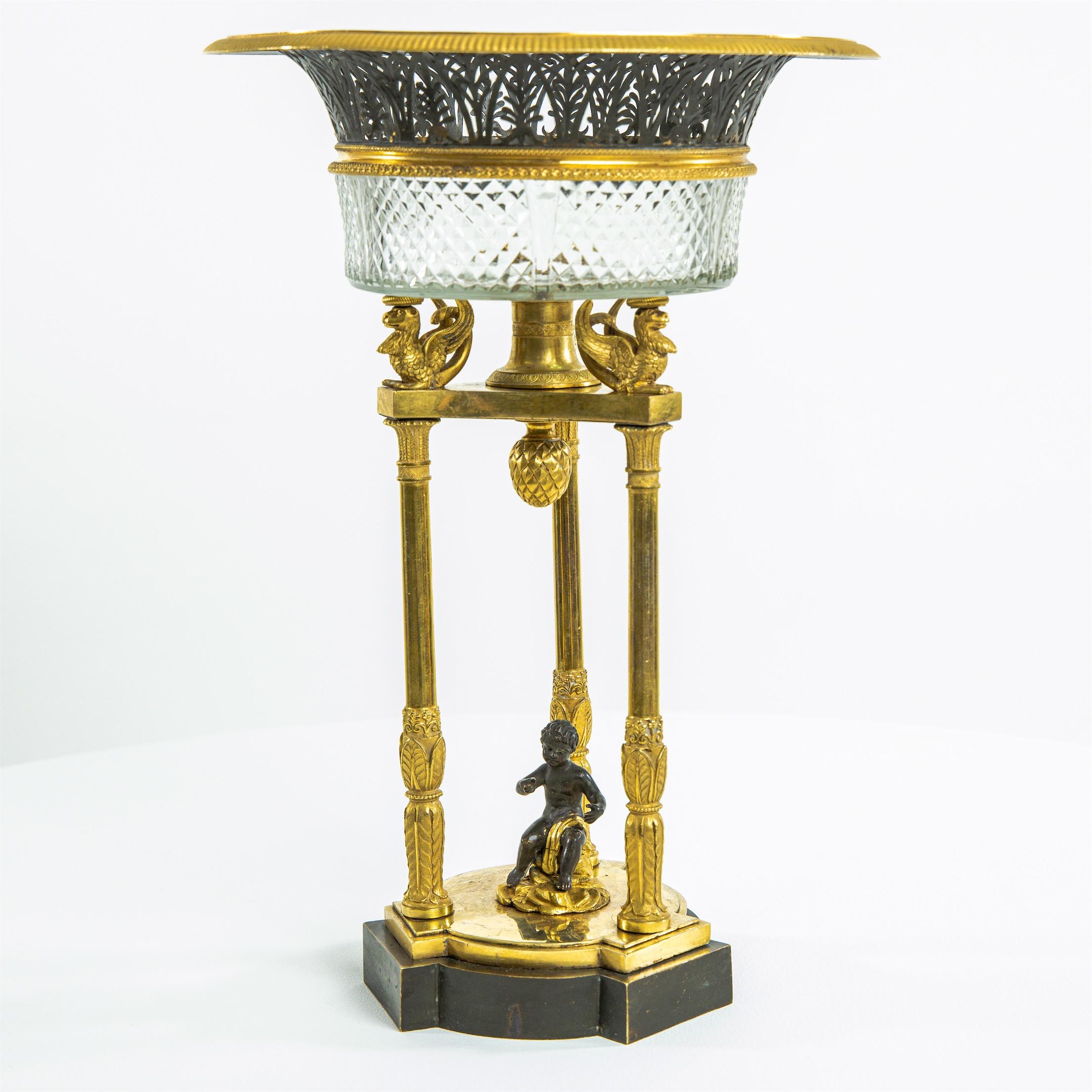 Empire centerpiece made of cut glass and fire-gilded bronze with griffin decor and small putto figure in the center.