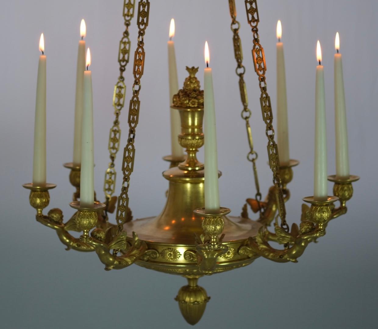 Kronleuchter aus vergoldeter Bronze mit acht Kerzenhaltern. Tolles Design mit geflügelten Putten, die die Urnen halten, in denen wiederum die Kerzen stehen. Gute Qualität und guter Zustand.