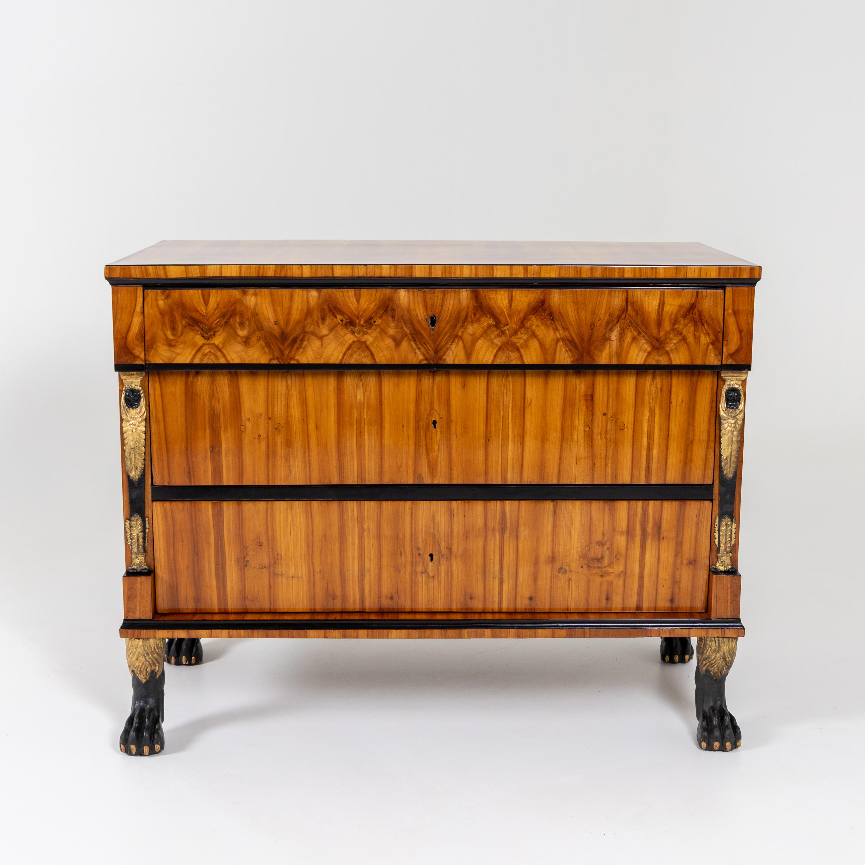 Empire chest of drawers standing on carved and partly gold-patinated paw feet with three drawers, ebonised traverses and profiles as well as flanking caryatids. Very beautiful cherry veneer, hand polished and restored.