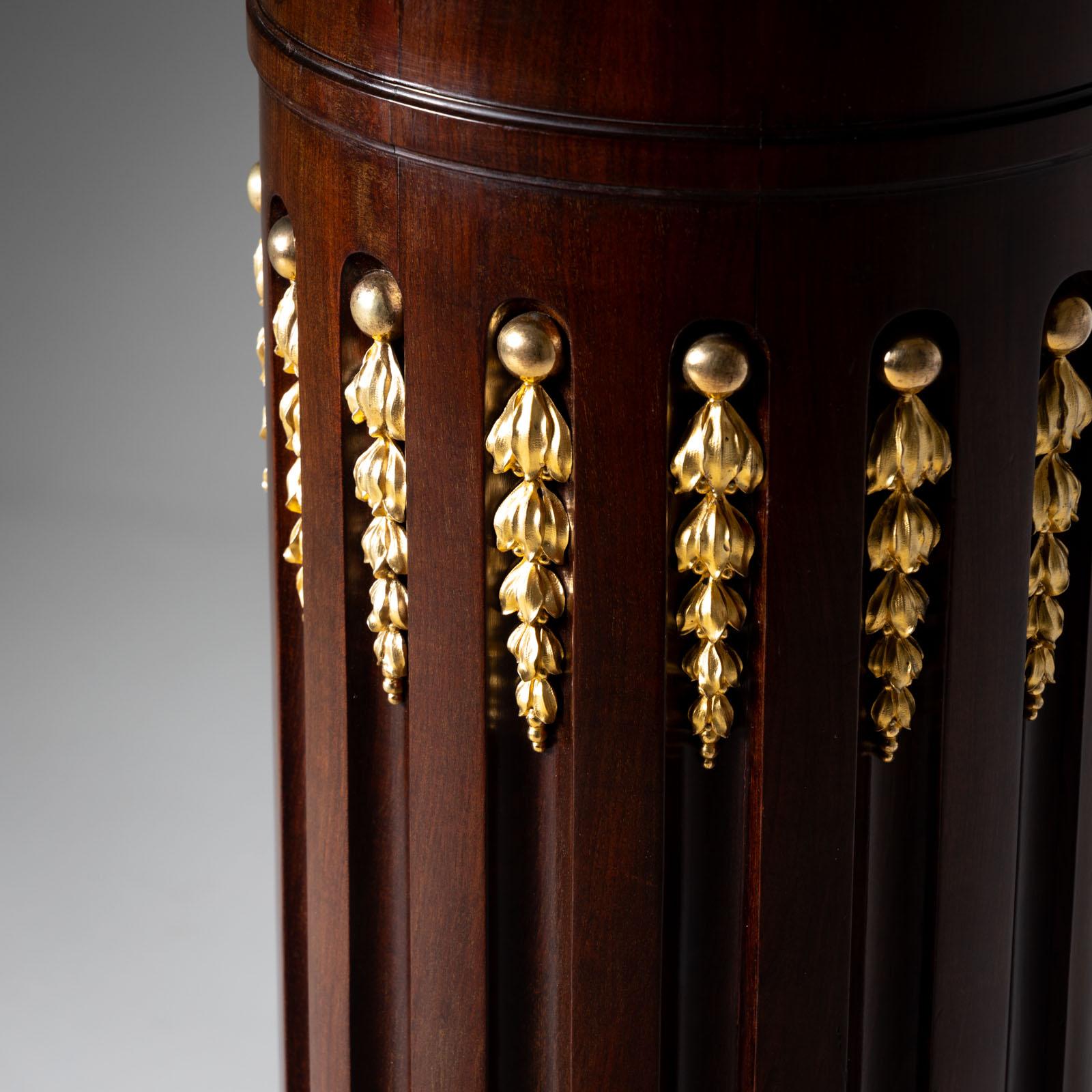 Fluted column in mahogany veneer, with a white marble top and fire-gilt appliqués in the fluting. The chest of drawers stands on a round, multi-profiled base over gilded paw feet. The diameter of the shelf is Ø33 cm. 