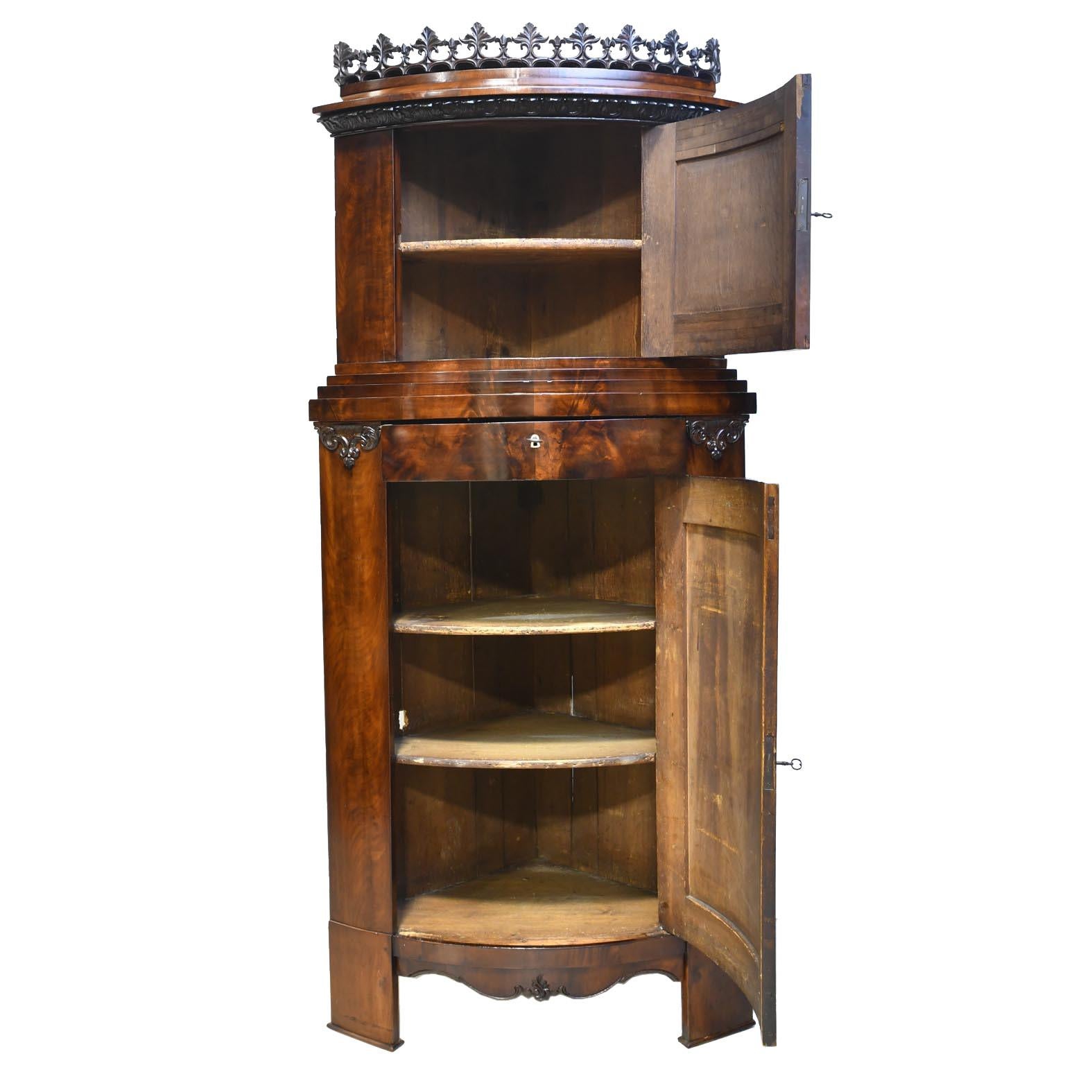 From the Baltic region, a very beautiful and unusual Empire corner cupboard in fine West Indies/ Cuban mahogany with two stacked cabinet doors that are bowed, and are separated by a drawer. Some distinctive architectural details include the finely